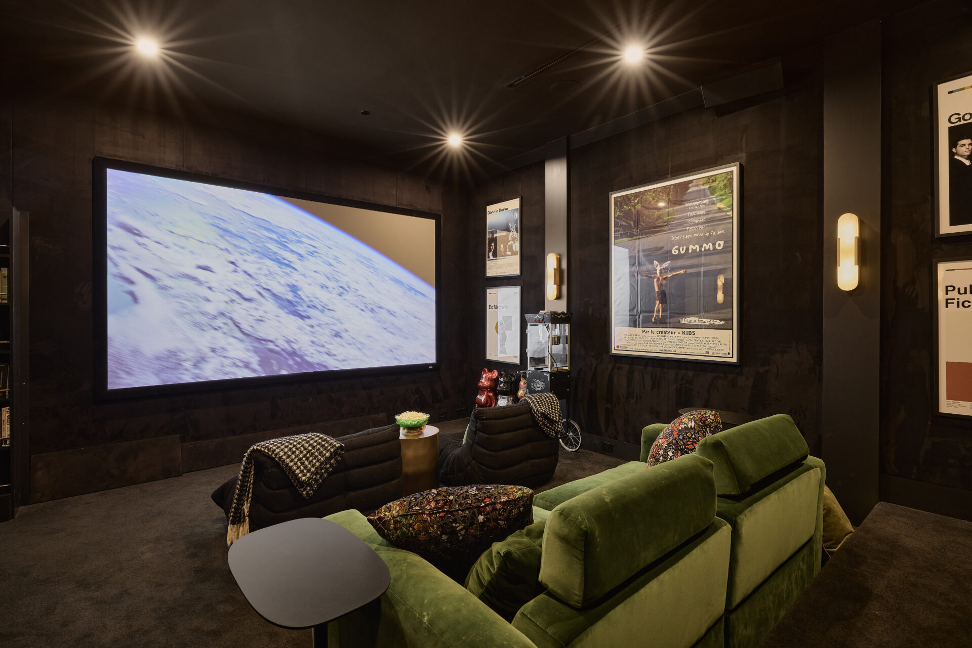 The hidden movie theater features with dark walls, plush seating, movie posters, and a massive screen.