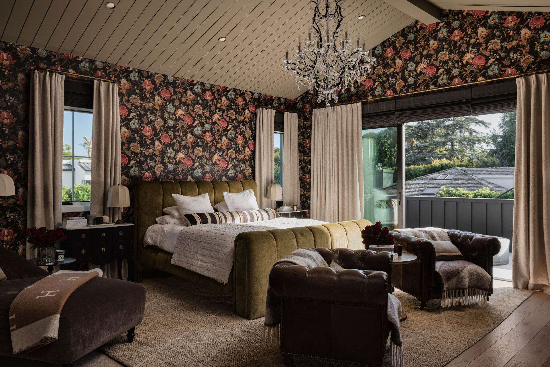 Bedroom centers around a plush upholstered bed wrapped in rich textures, framed by bold, flower wallpaper that adds visual depth. 
