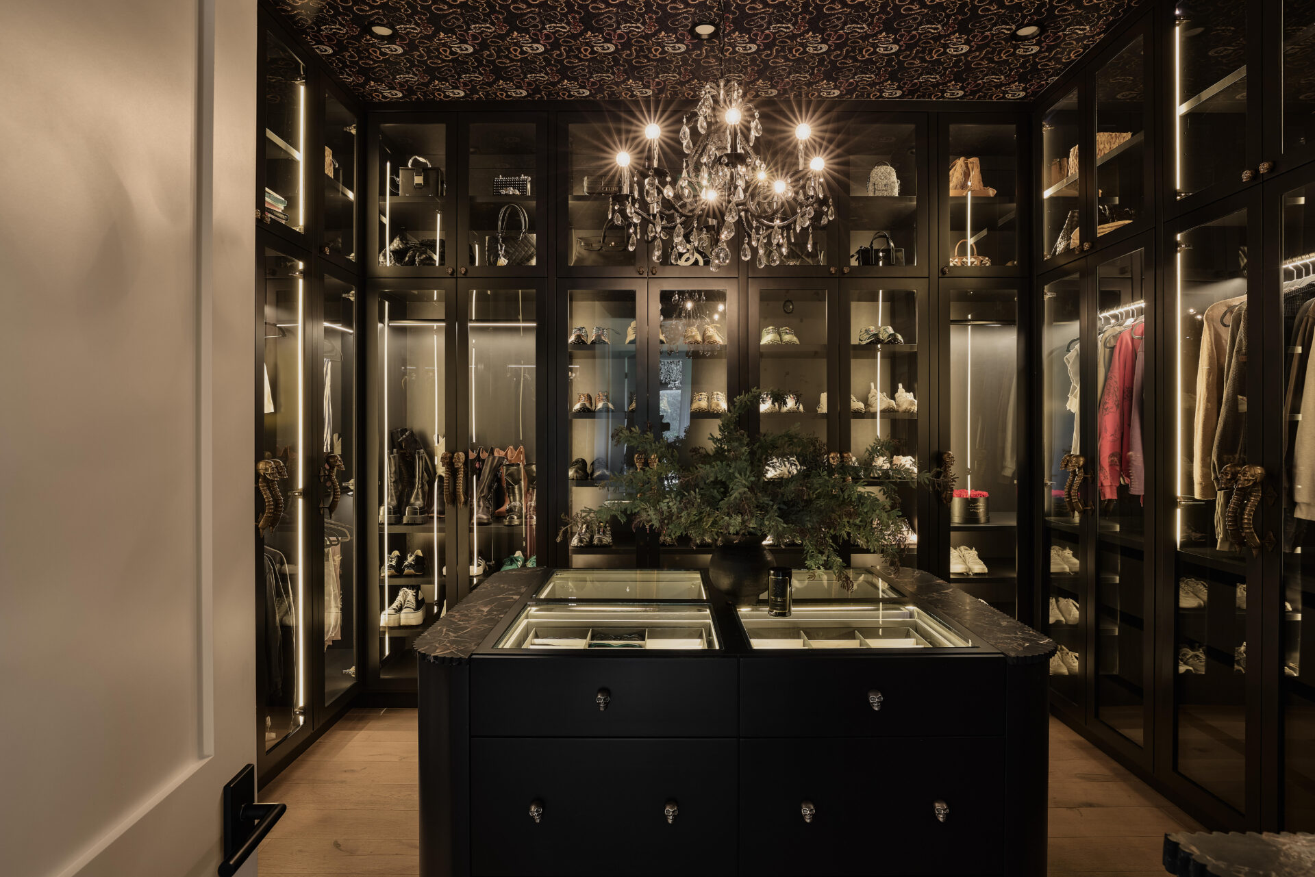 A walk-in closet lined with floor-to-ceiling glass-fronted cabinetry to display shoes, handbags, and clothing.