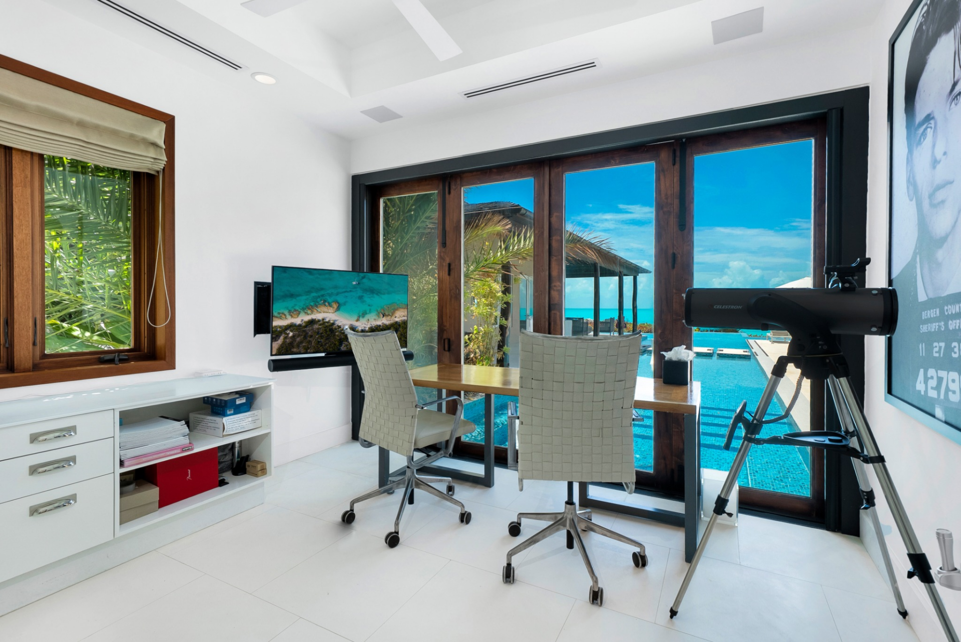 The office is positioned to capture direct views of the pool and ocean, with a clean-lined desk setup framed by floor-to-ceiling glass.