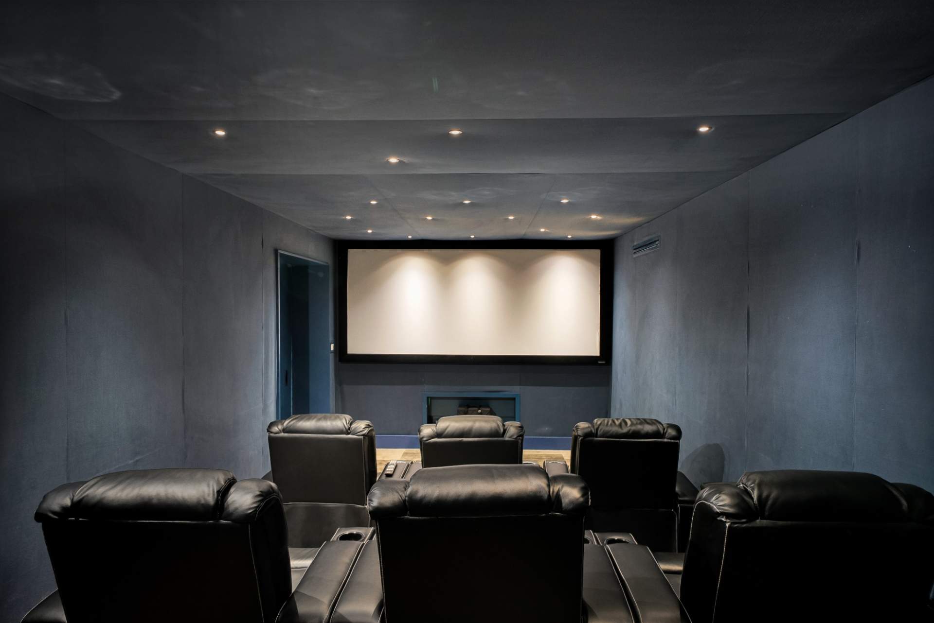 The private cinema is wrapped in dark, sound-treated walls with tiered leather recliners facing a full projection screen.
