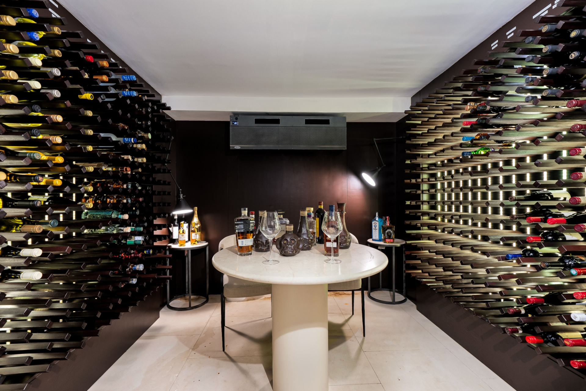Wine cellar lined with illuminated bottle racks on both sides that frame a central tasting table.