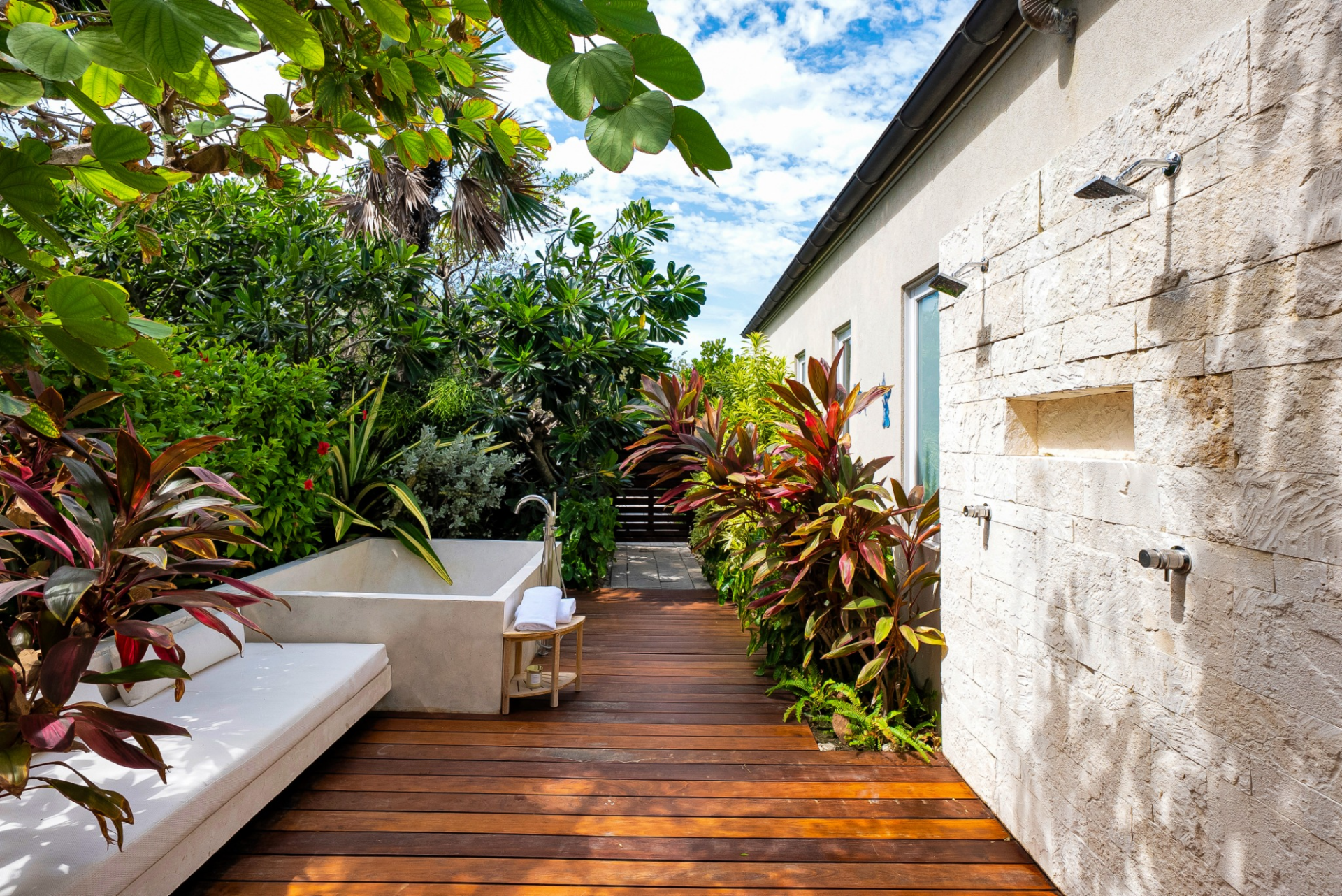 Tucked within the tropical landscaping, the outdoor bath and dual showers are wrapped in stone and wood, creating a private, spa-like space hidden from the rest of the estate.