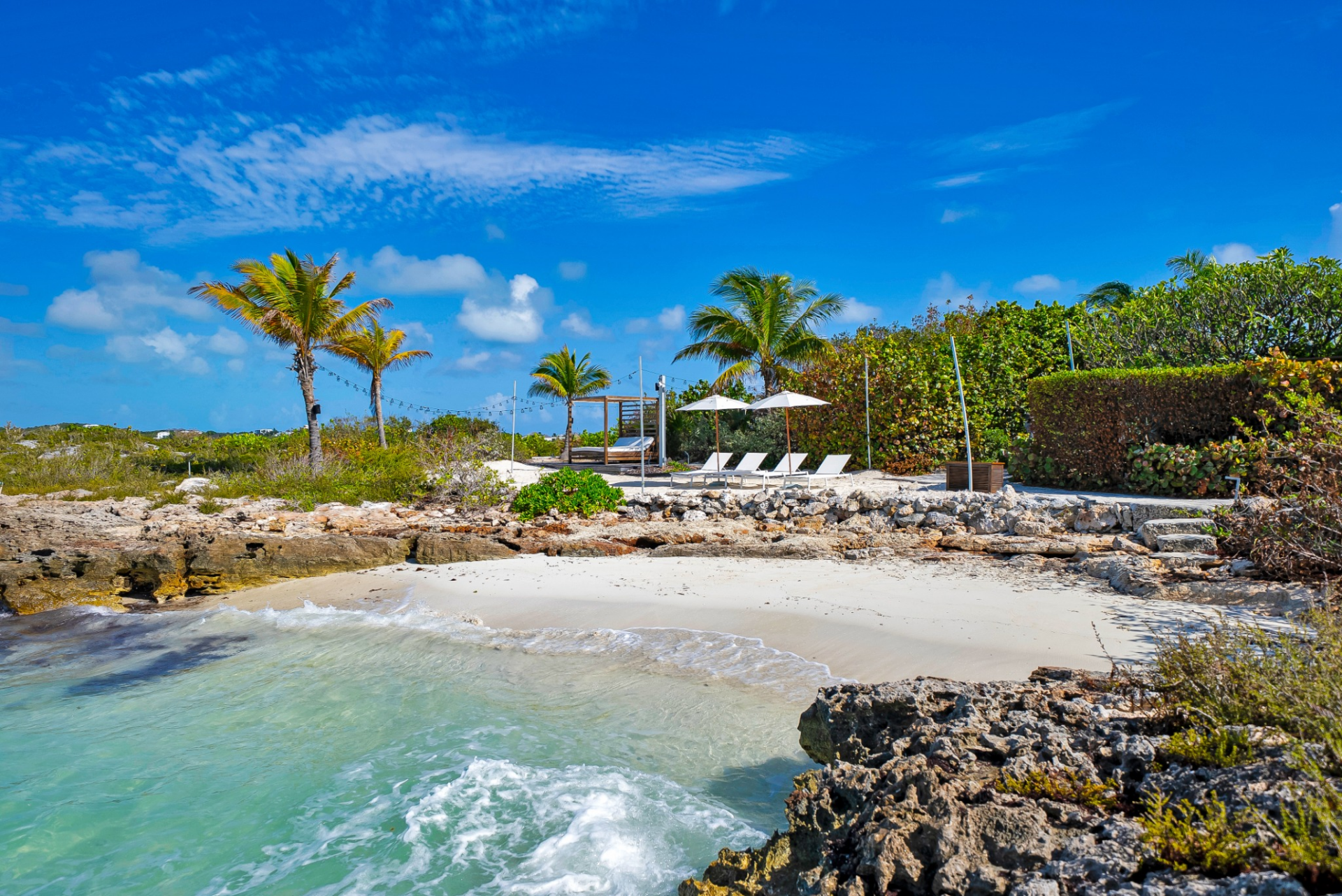 Cabana-lined shoreline features a raised wooden deck with a shaded daybed, positioned just above the sand.