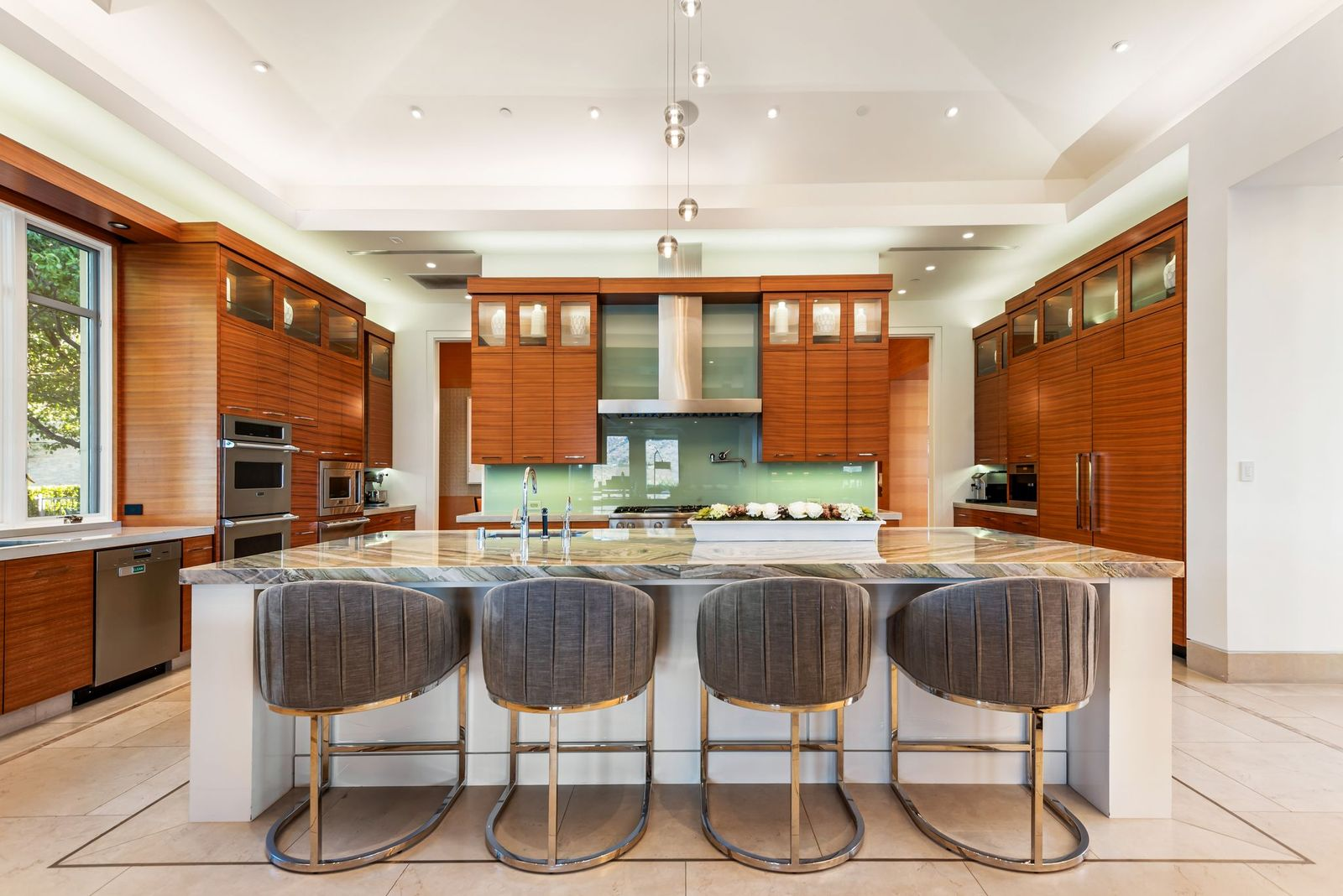 A large central island in the kitchen is topped in polished stone and lined with seating, while clean-lined cabinetry and integrated appliances line the walls.