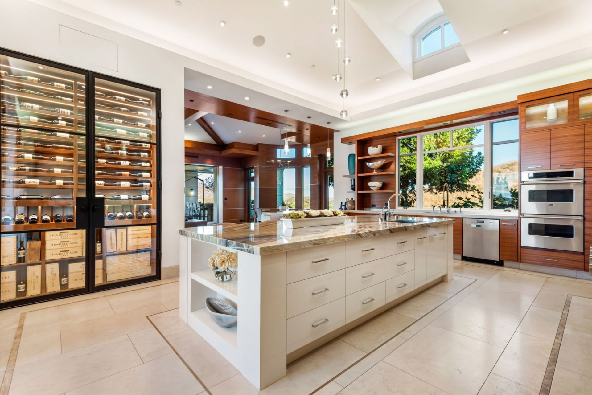 A glass enclosed wine wall sits to the left and the main sink sits on the right beneath a window in the kitchen.