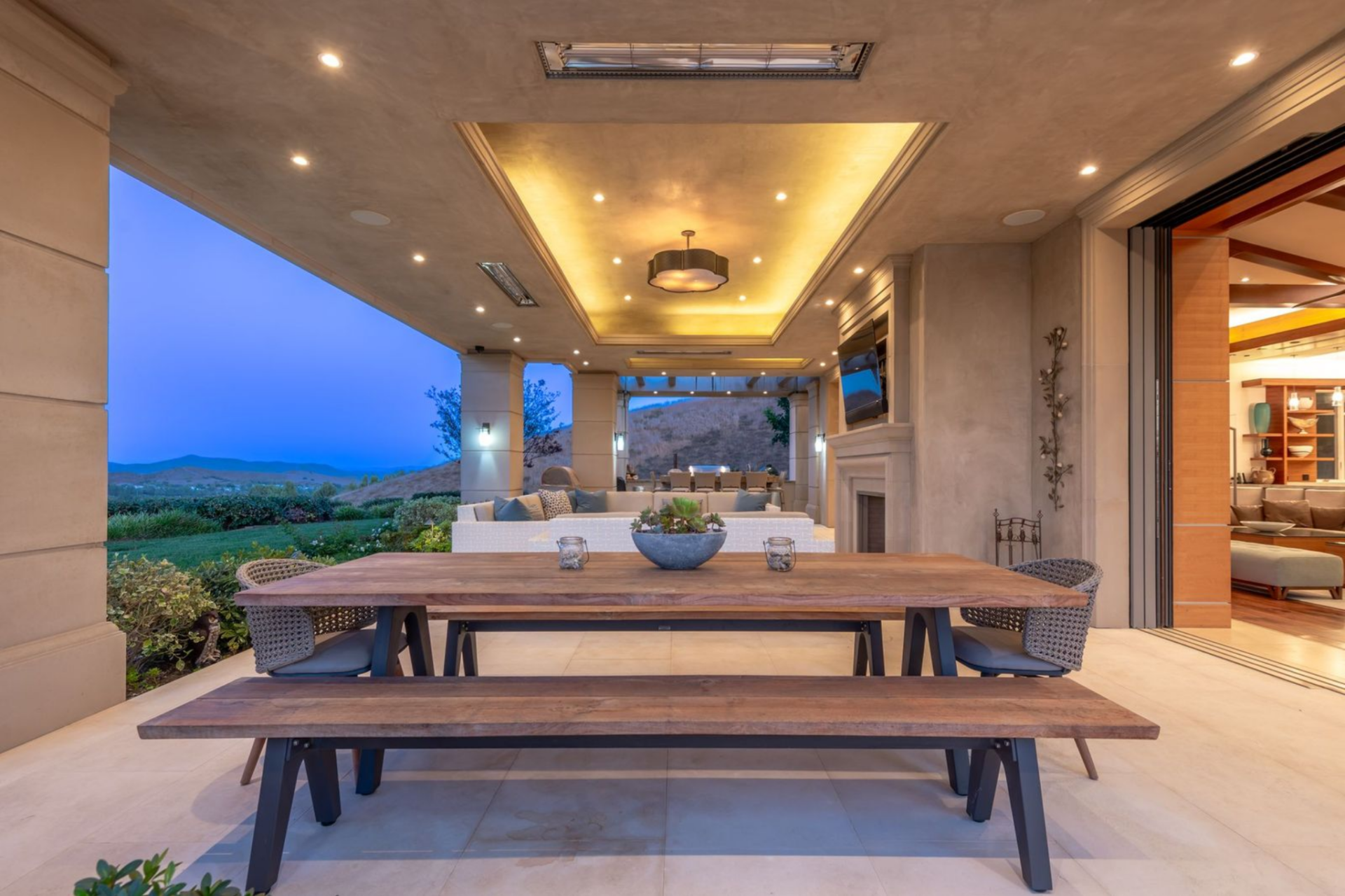 The outdoor living room is framed by stone columns and warmed by recessed lighting set into the ceiling.