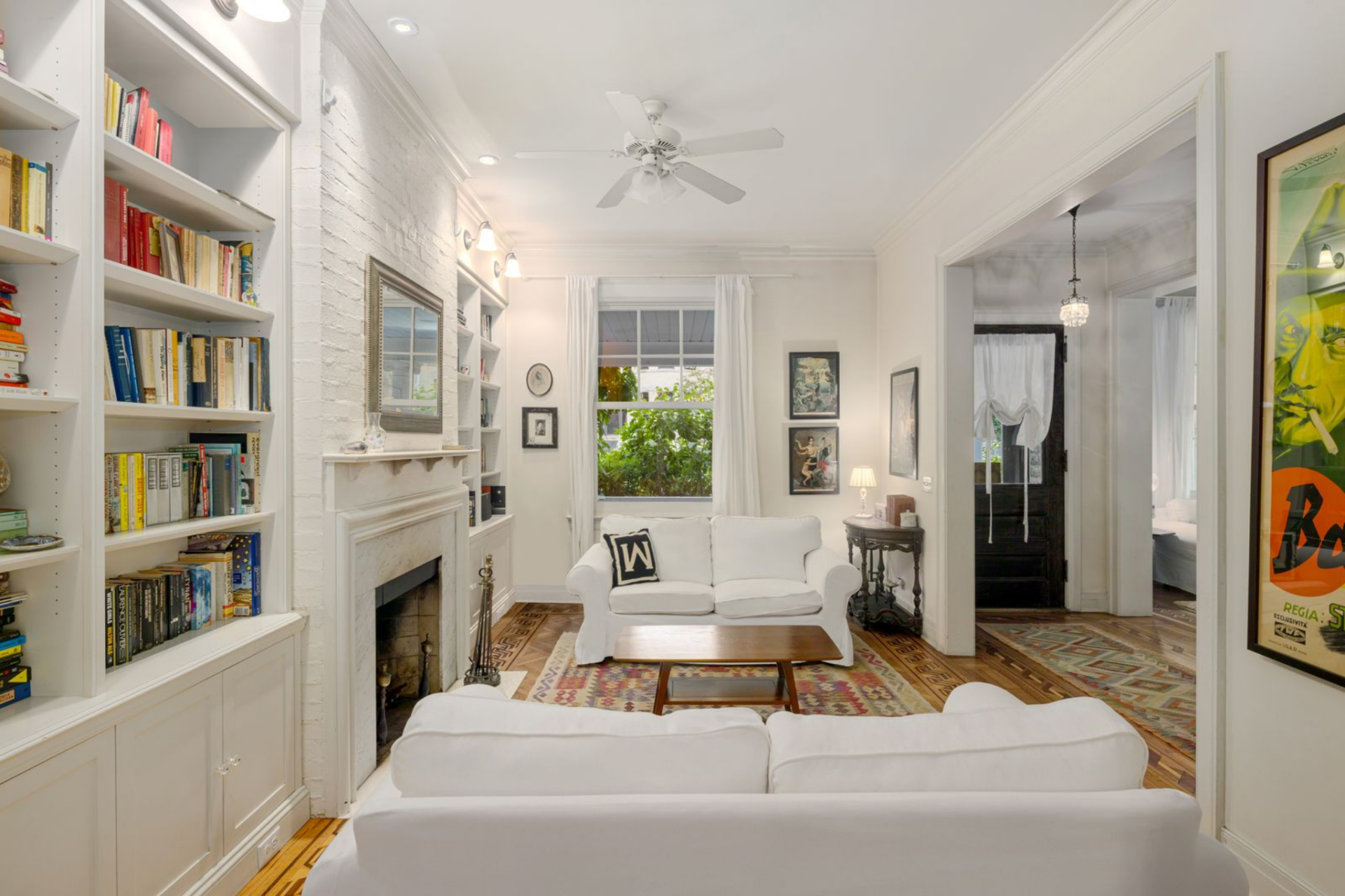 White-upholstered seating is arranged directly across from the fireplace, while a patterned area rug introduces warmth against the hardwood floors. 