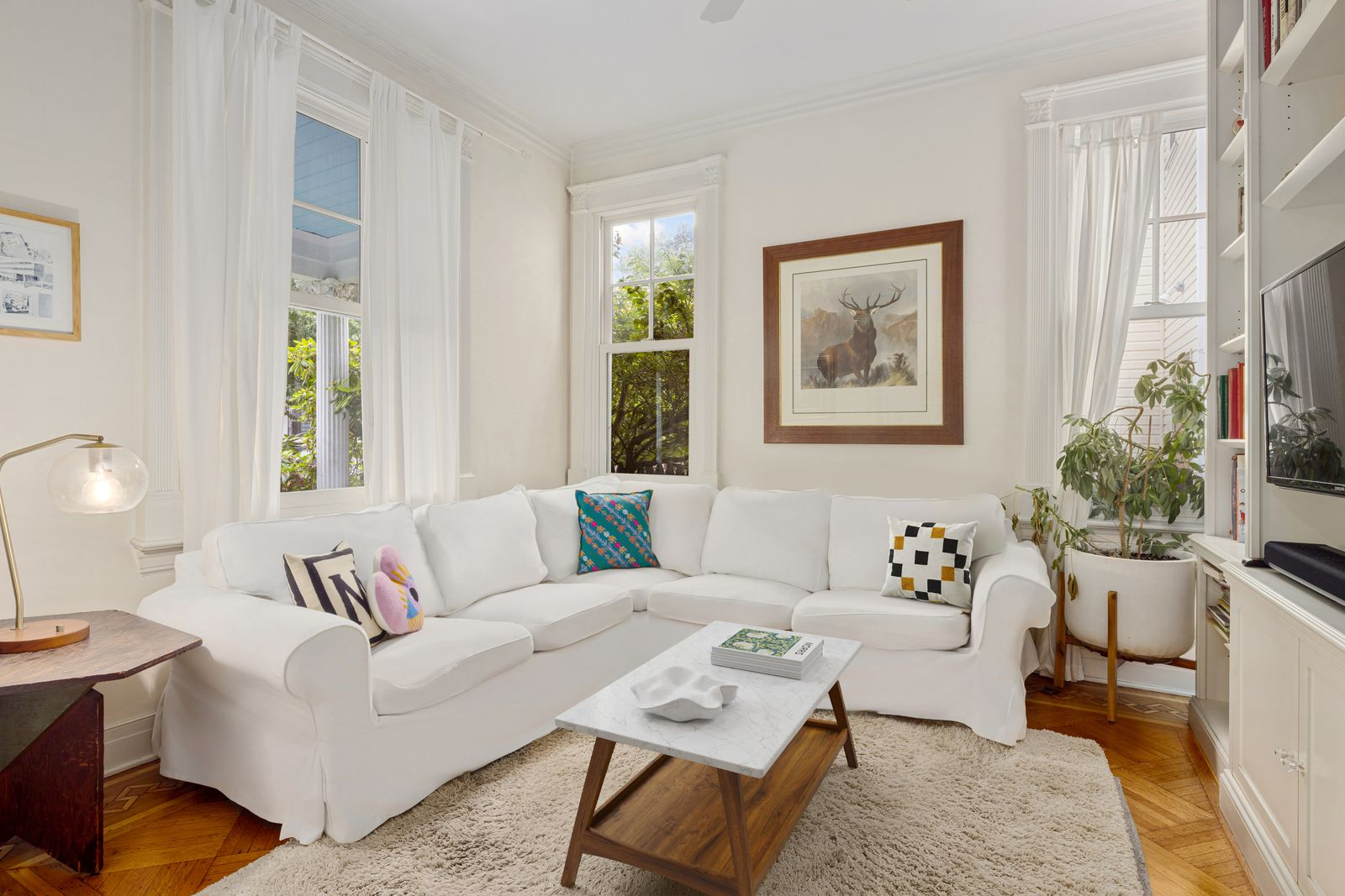 A den organized around a large, white sectional tucked into the corner of the space, with a simple wood coffee table and textured area rug in the center of the room. 