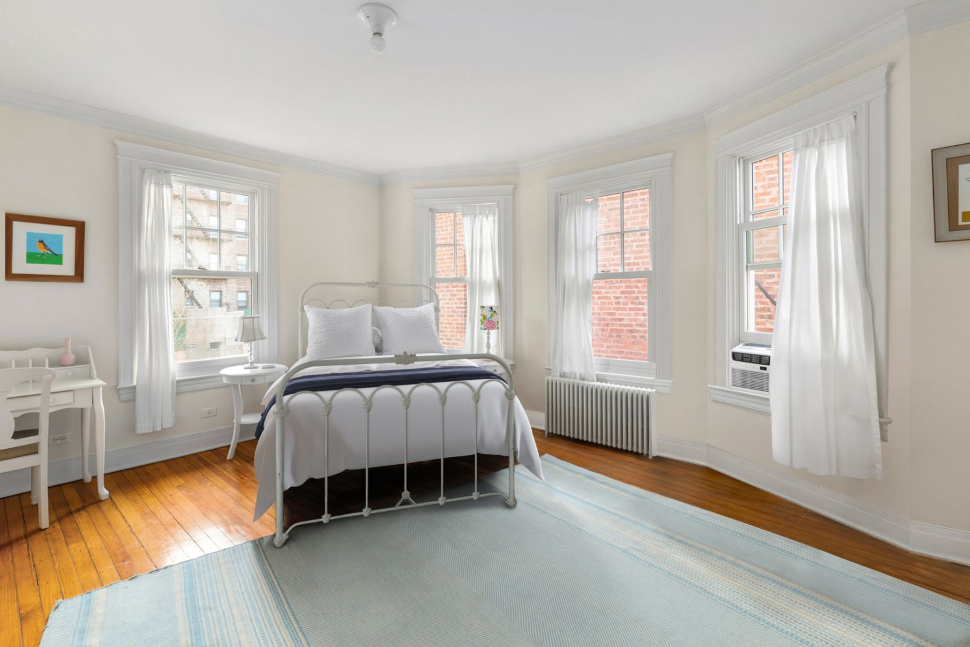 Bedroom sitting along a bay of tall windows with white-painted trim, hardwood floors, and soft wall tones.