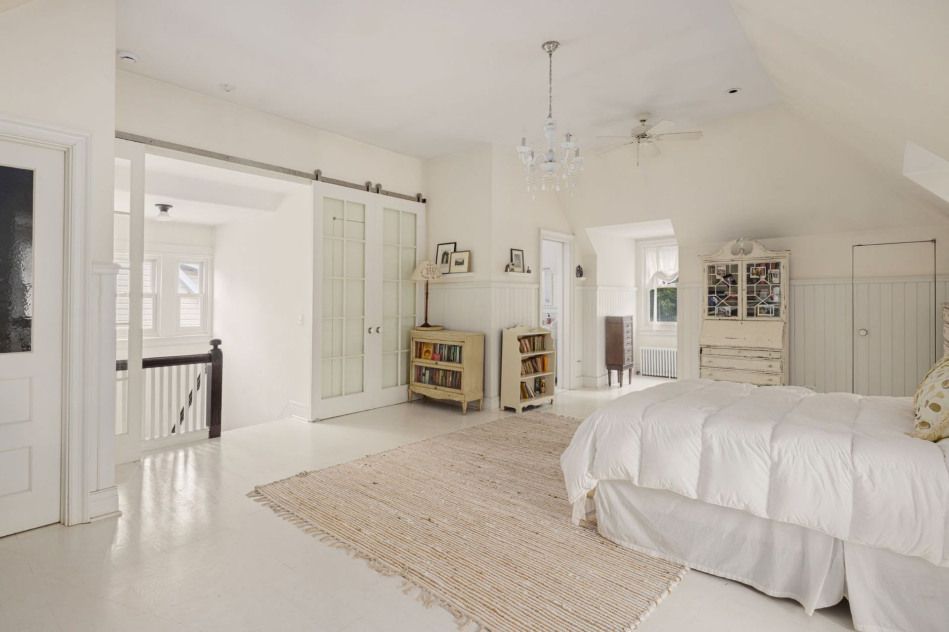 Loft-like suite with painted white floors, beadboard paneling, and soft architectural cutouts give the room attic-style character.