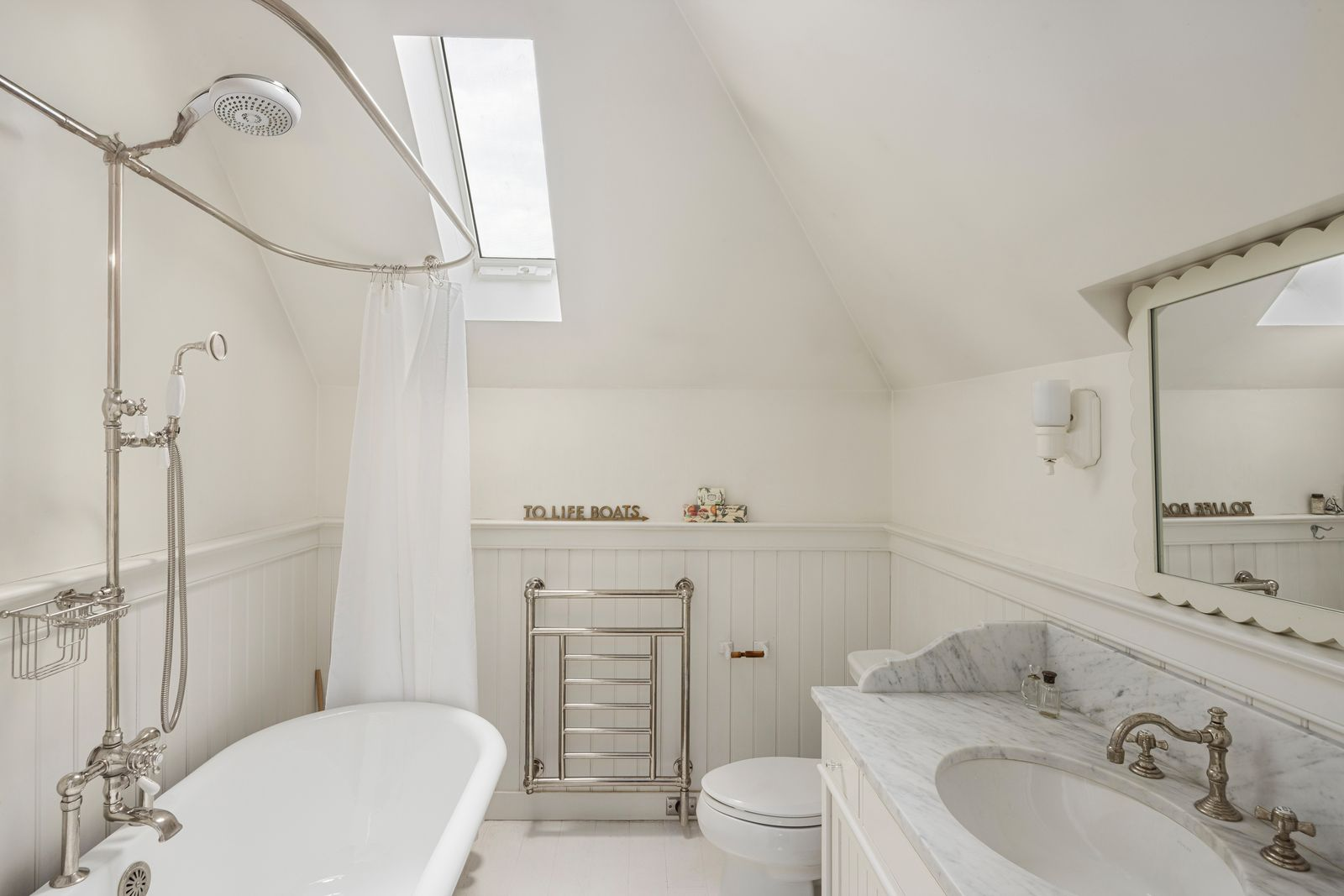 Bathroom with a marble-topped vanity, vintage-style fixtures, and a freestanding tub tucked beneath an angled skylight. 