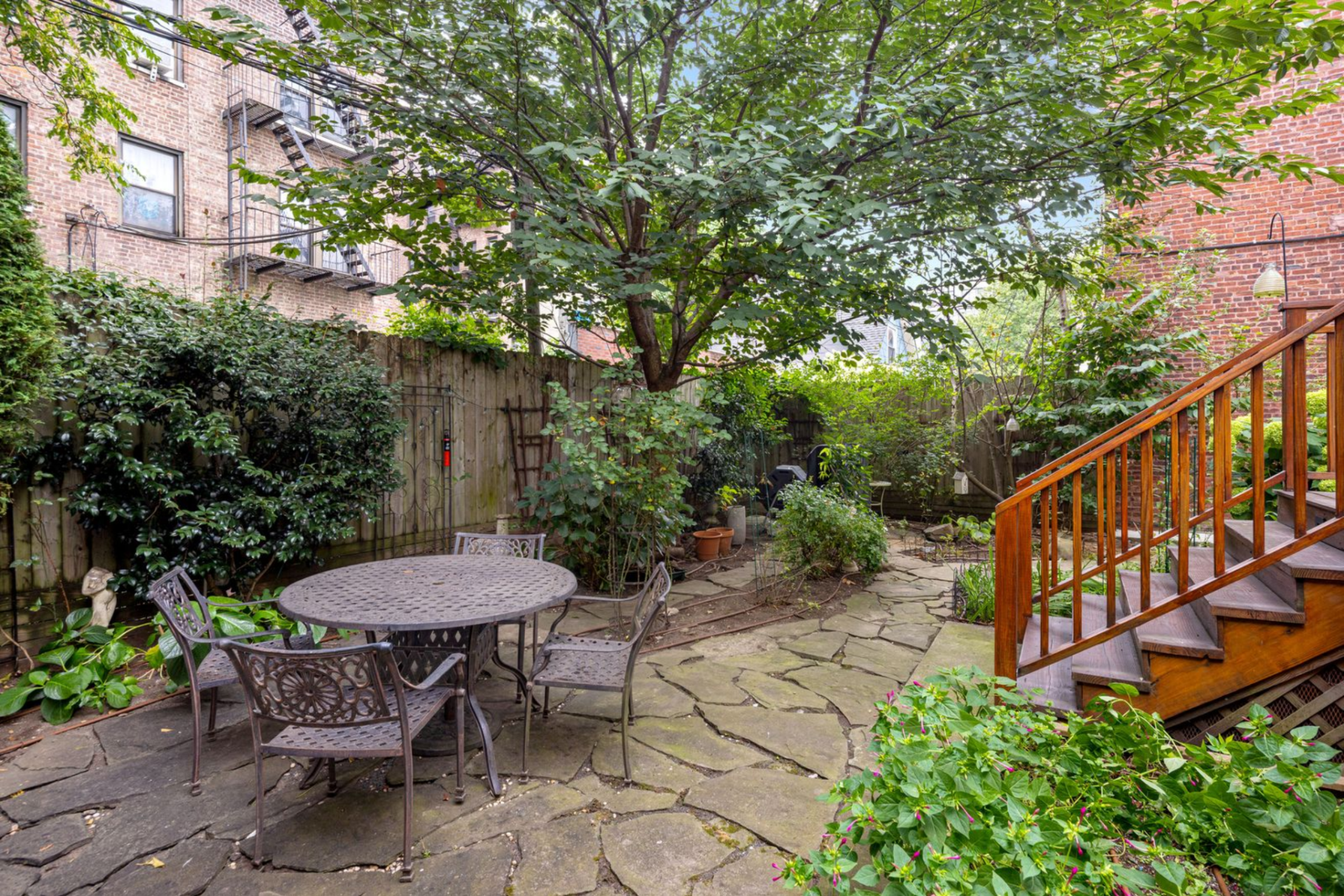 From the deck, a short set of stairs leads down into the garden, where the space opens into a paved stone patio with a metal table and chairs.
