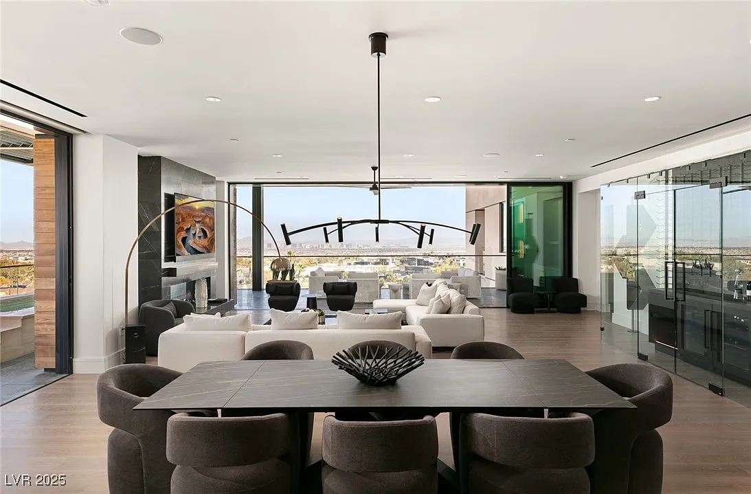 Behind the living room is a dining area with a long rectangular black table beneath a linear light fixture.