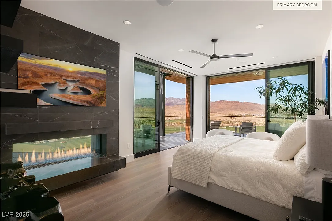 The primary bedroom is anchored by a full-height stone fireplace wall, finished in dark slab stone with a linear gas insert opposite the bed. 