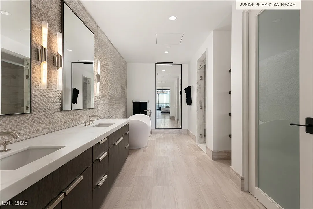 En-suite bathroom is laid out in a long horizontal layout with textured wall tile and pale stone flooring. 