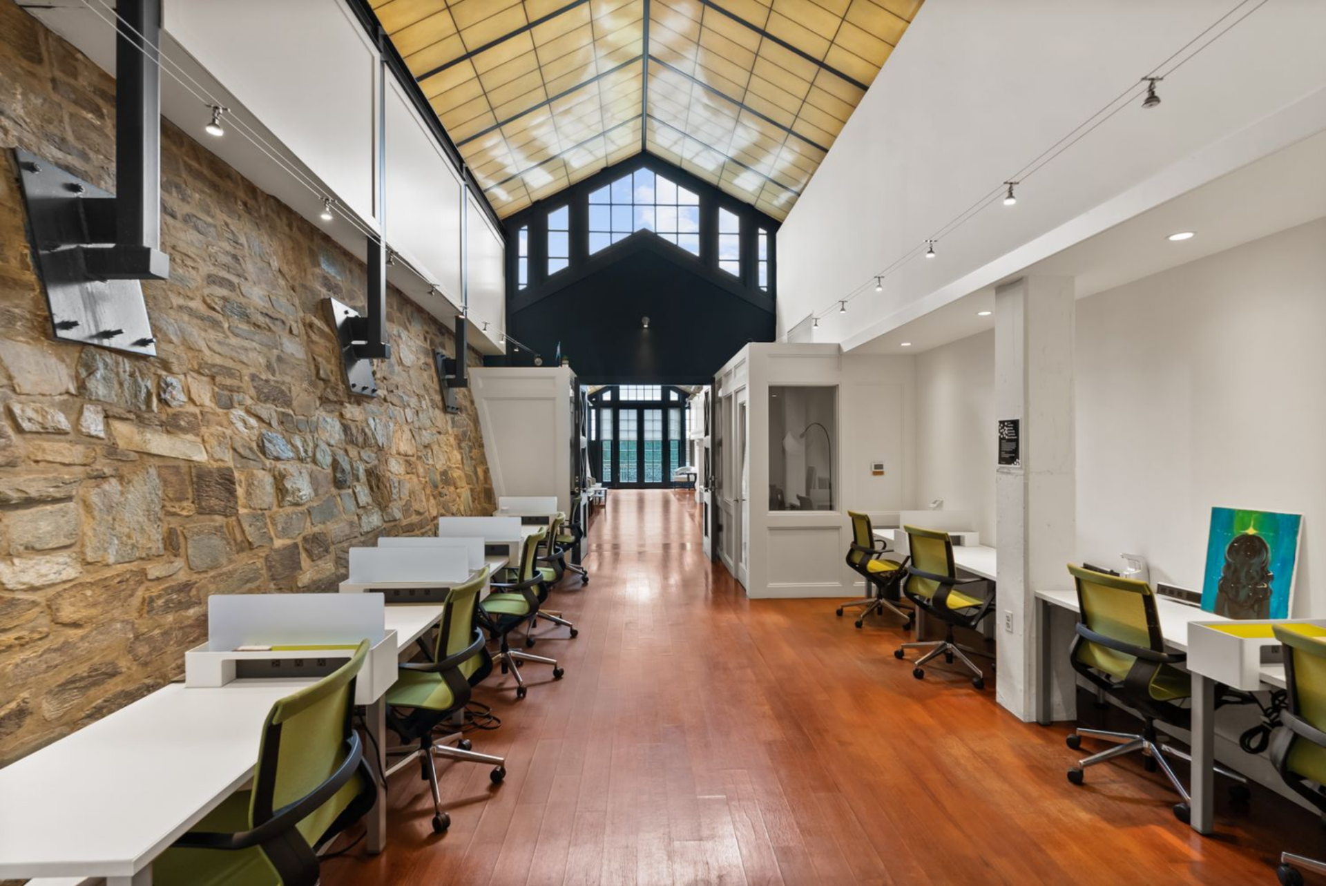 A long row of workstations arranged parallel to a stone wall, with warm wood floors running beneath exposed beams and a vaulted ceiling overhead.
