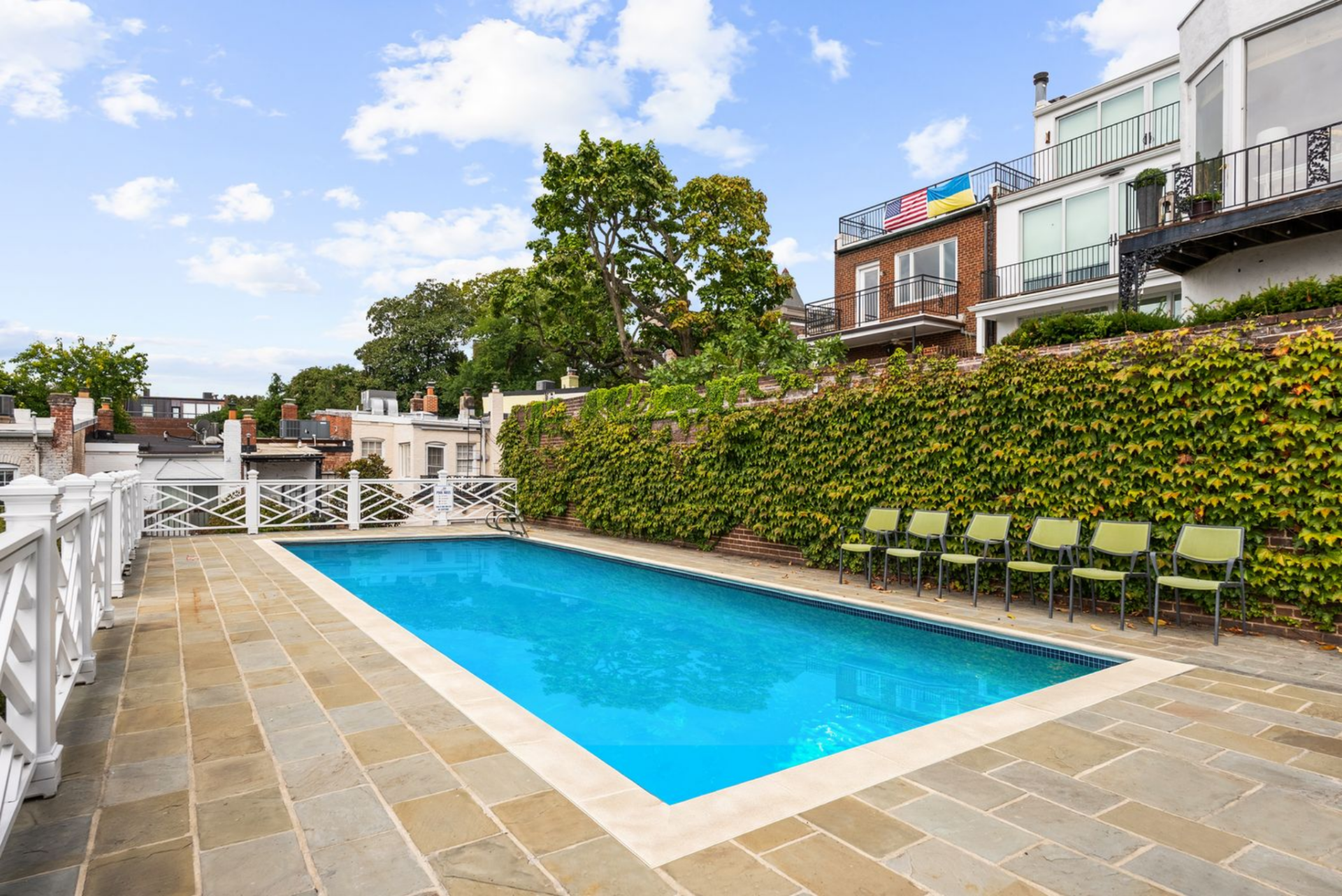 A rectangular swimming pool bordered by stone pavers and ivy-covered walls, with a row of chairs lining the edge, creating a clean, structured finish to the garden.