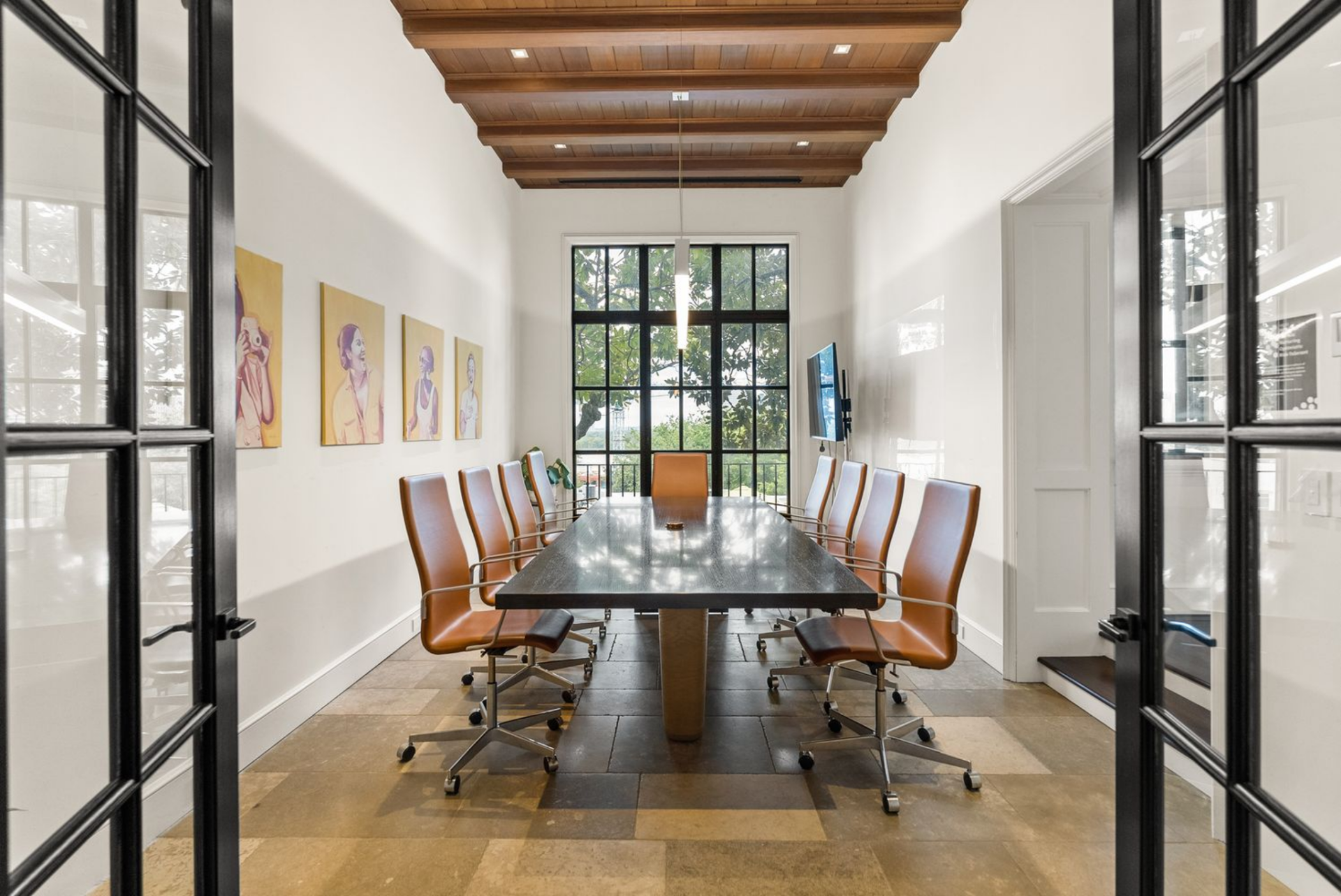 Conference room with a rectangular table and rolling leather chairs arranged beneath a beamed wood ceiling. 