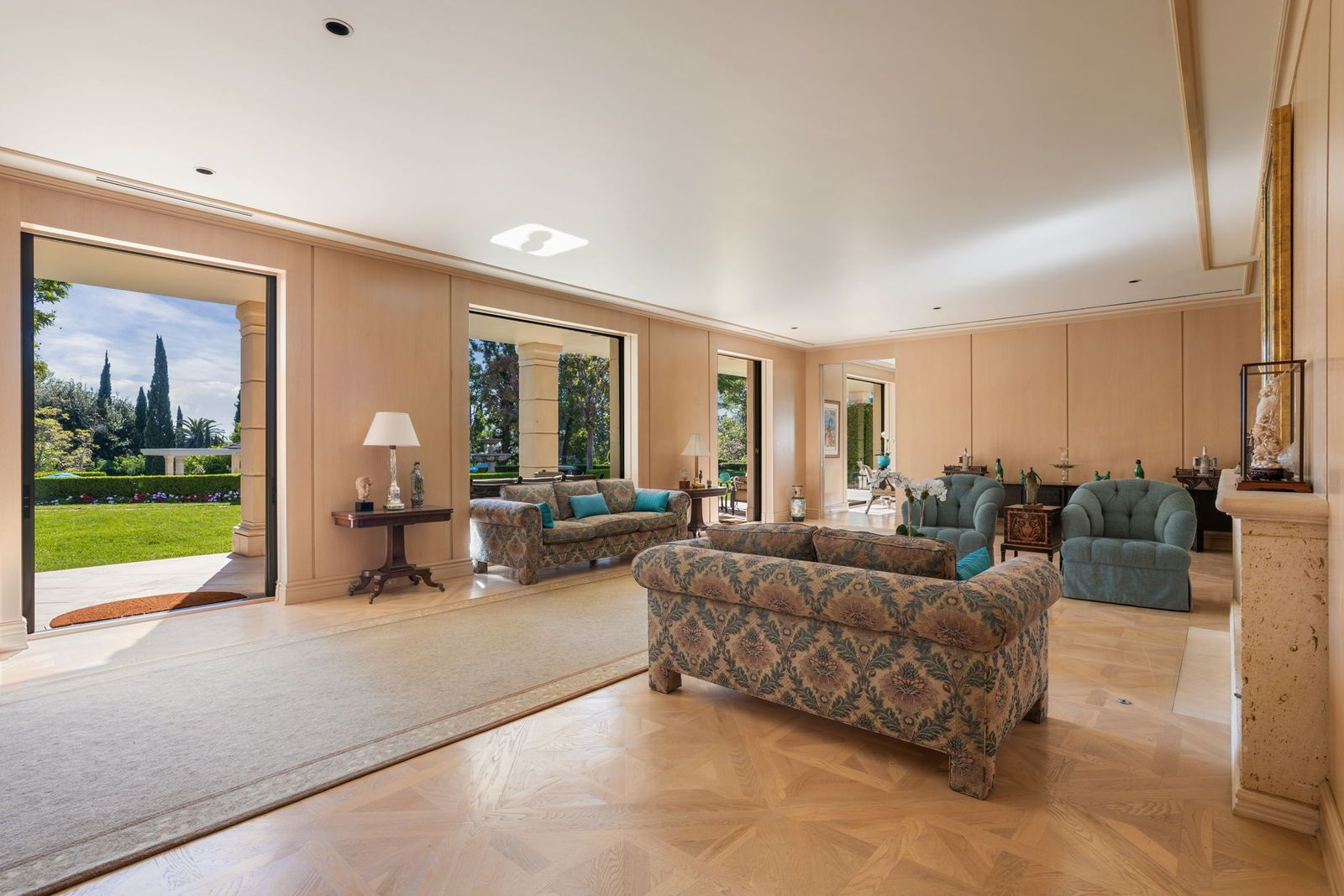 Great room with pale wood floors laid in a geometric pattern beneath vintage patterned couches and blue armchairs.