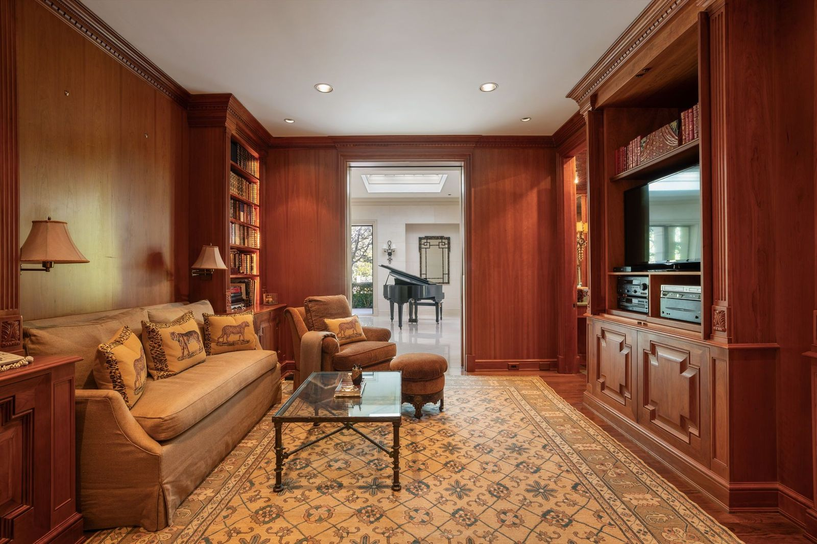 Wrapped in rich wood paneling, the den features floor-to-ceiling shelving that frames the room, combining open bookcases with enclosed cabinetry that houses media components and an extensive library. 