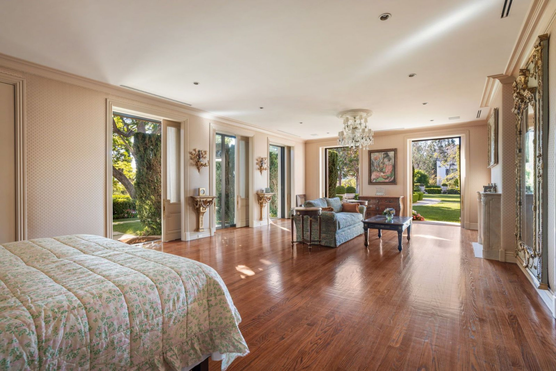 Bedroom that opens wide with polished wood floors, tall windows, and multiple sets of doors that connect directly to the surrounding gardens, allowing the room to extend outward on all sides. 