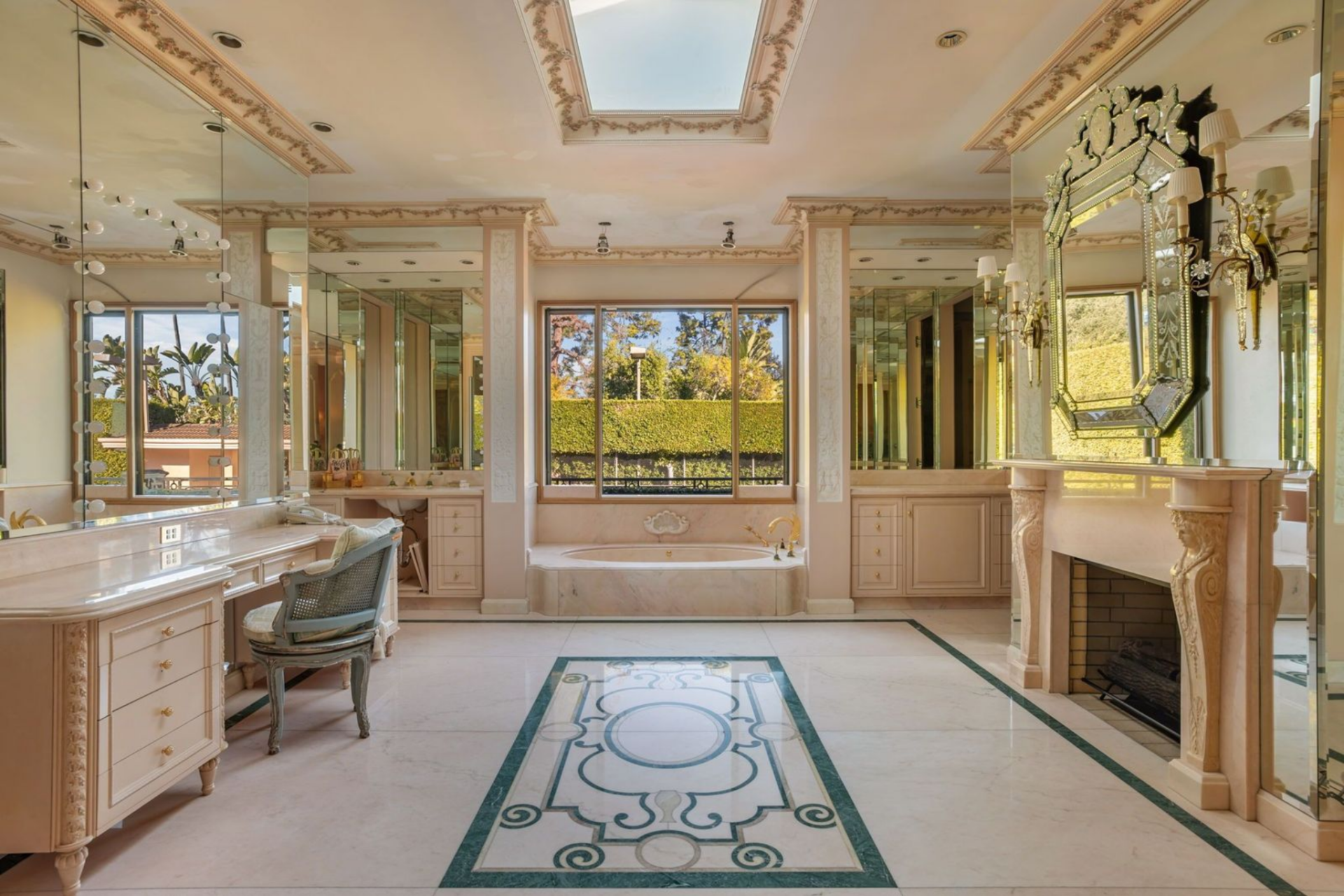 A large soaking tub is centered beneath a broad window, framed by mirrored walls and detailed molding that reflect both natural light and the garden.