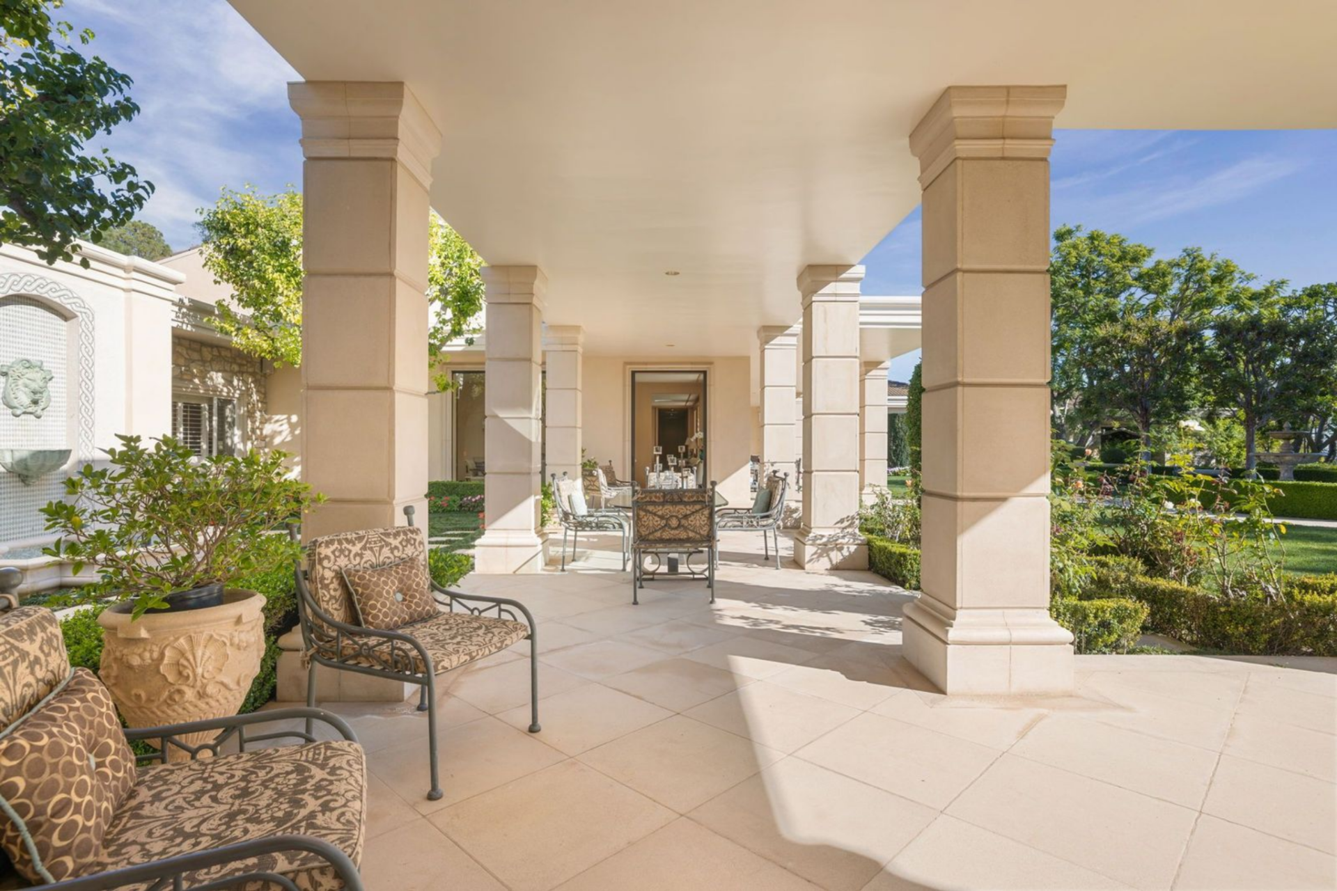 Supported by stone columns and finished in matching limestone flooring, the covered loggia offers shaded seating areas that overlook the grounds.