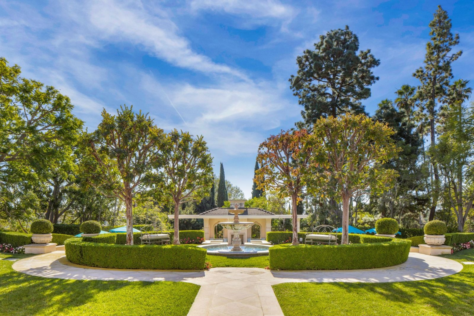 A central pathway leads to a tiered fountain courtyard, framed by clipped hedges and tall trees. 