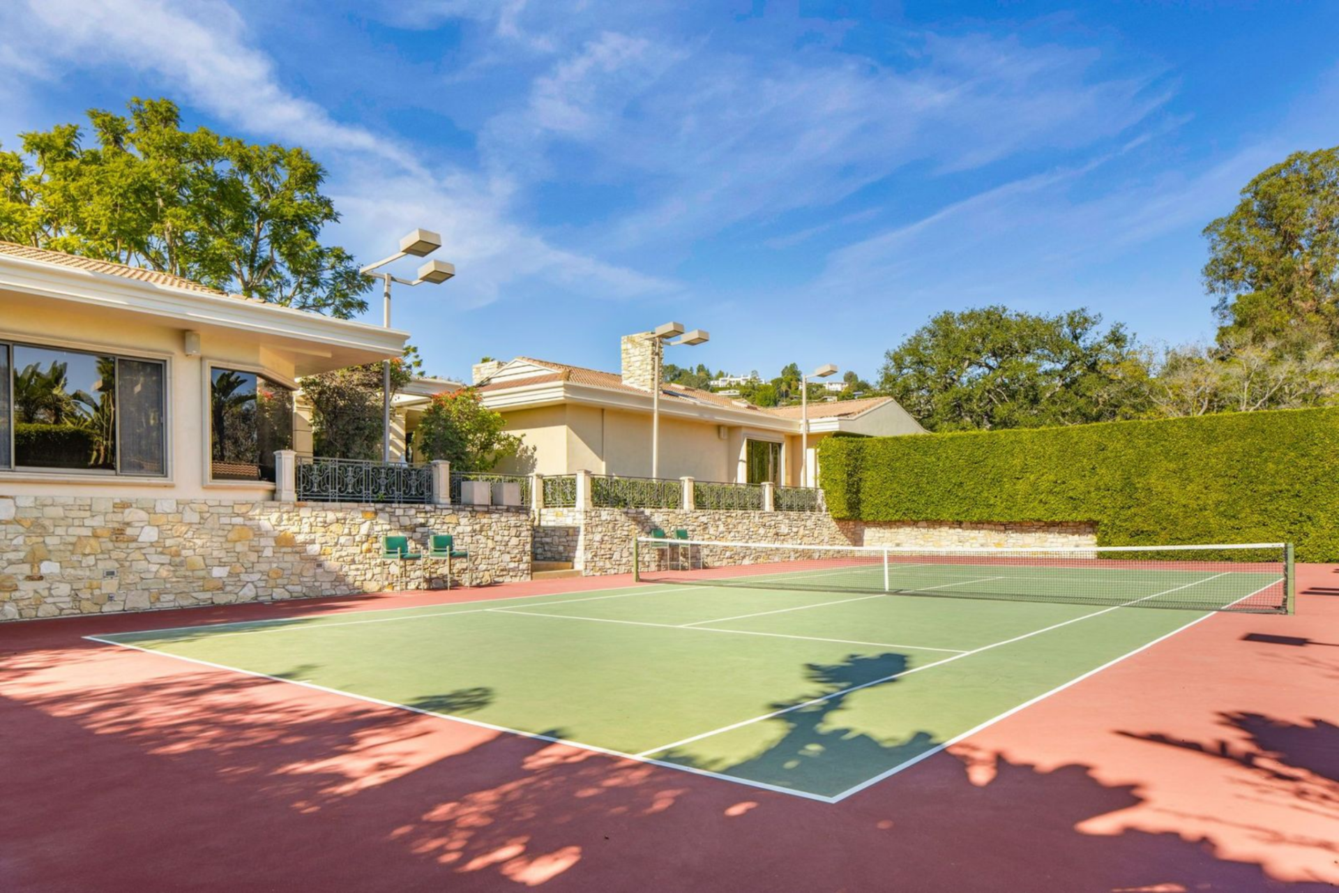 Large tennis court surrounded by hedges and a pavilion.