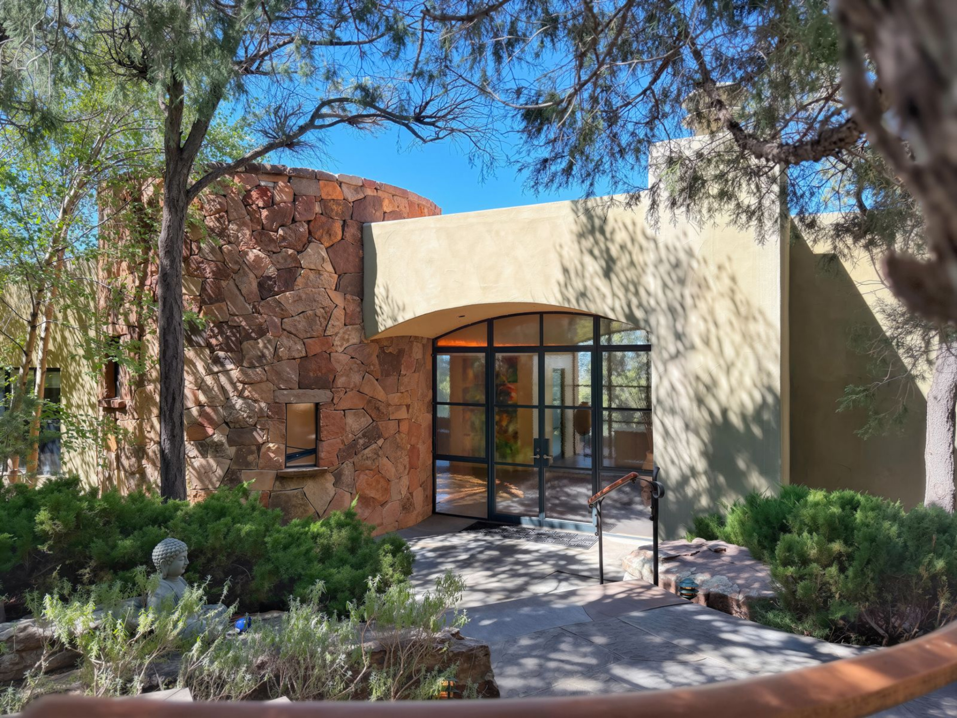 As you walk up to the house, a quiet path leads you toward a curved stone wall, where rough-cut rock and soft stucco wraps the exterior.