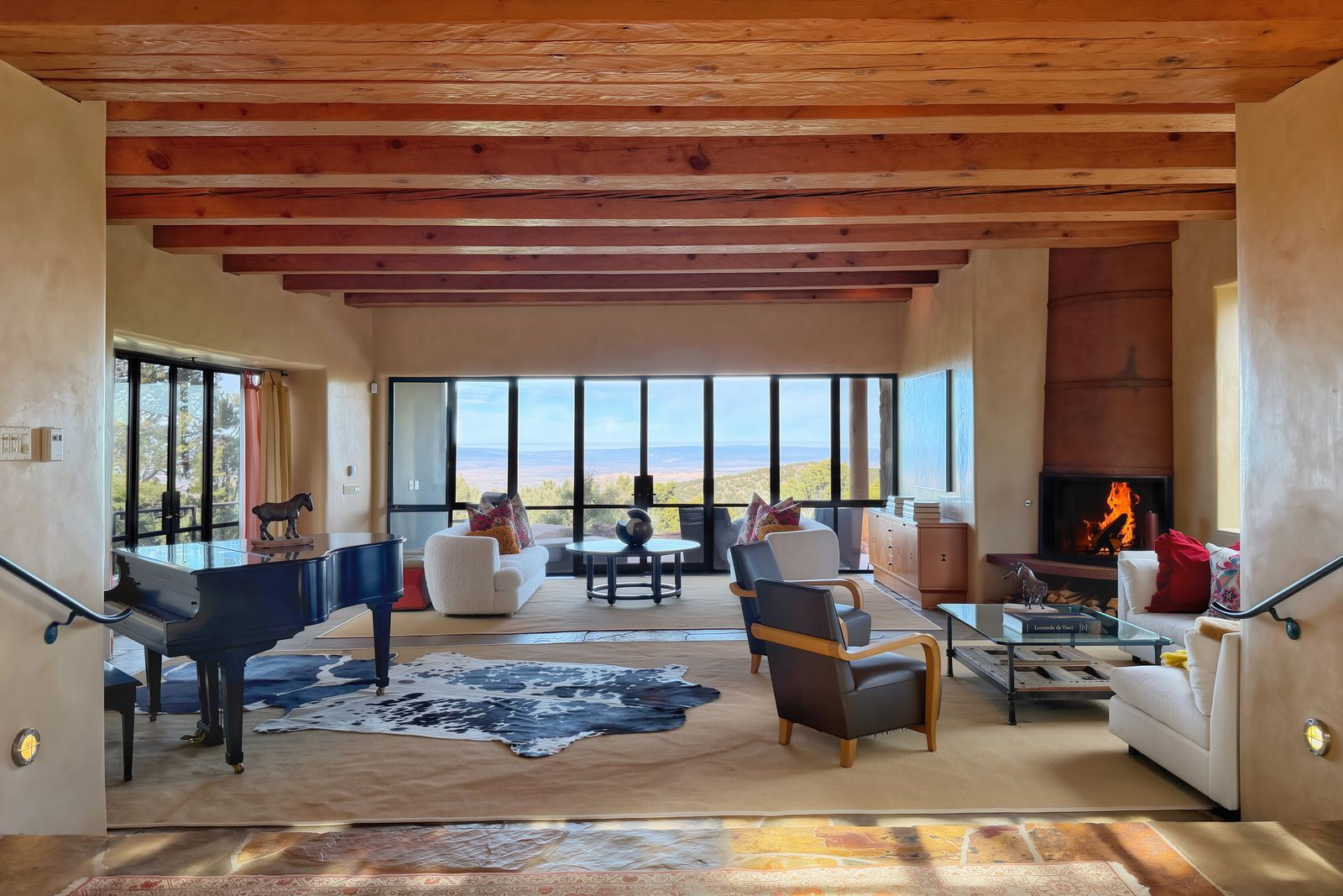 Living room set beneath exposed wood beams drawing your eye to a wall of glass that frames wide-open views of mountains.