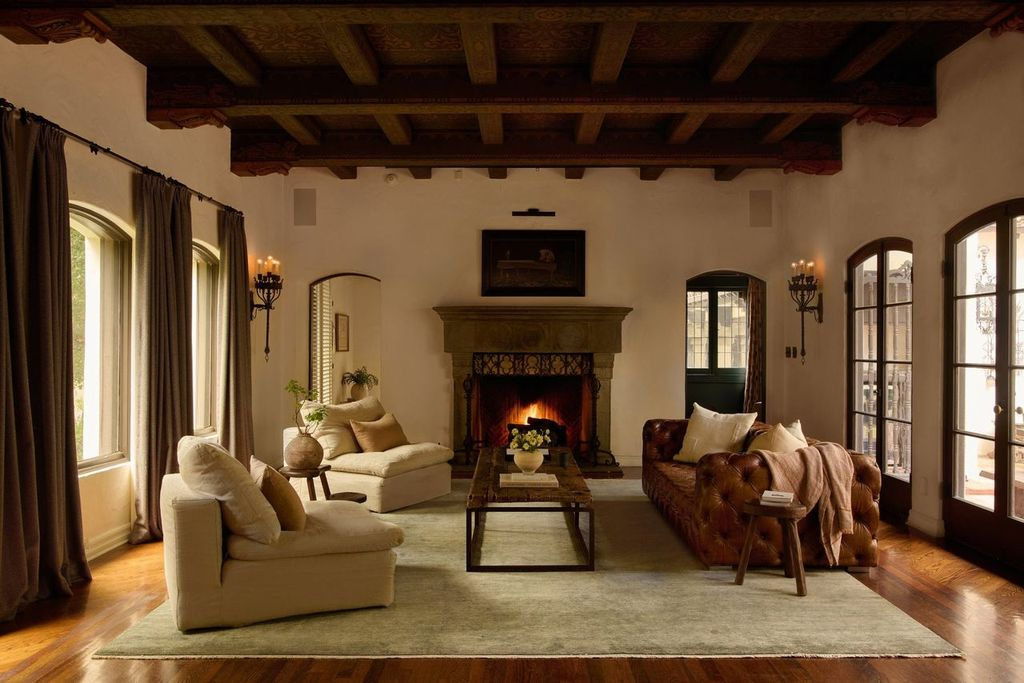 A fireplace sits in the center of the living room, framed by arched windows and French doors that pull in soft natural light and connect the room to the outdoors. 