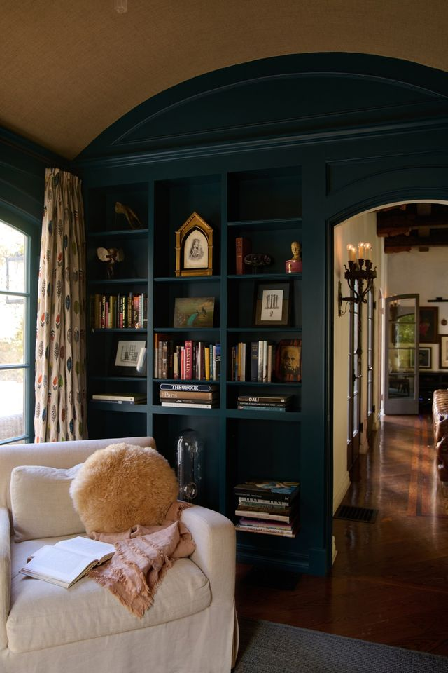 The arched doorway and curved ceiling keep the Spanish design consistent, while layered books, art, and collected objects add personality and lightness to the space.