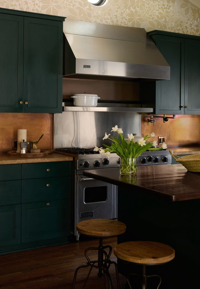 The updated eat-in kitchen blends classic character with thoughtful modern touches, centered around more deep green cabinetry, open shelving, and a professional-grade range. 