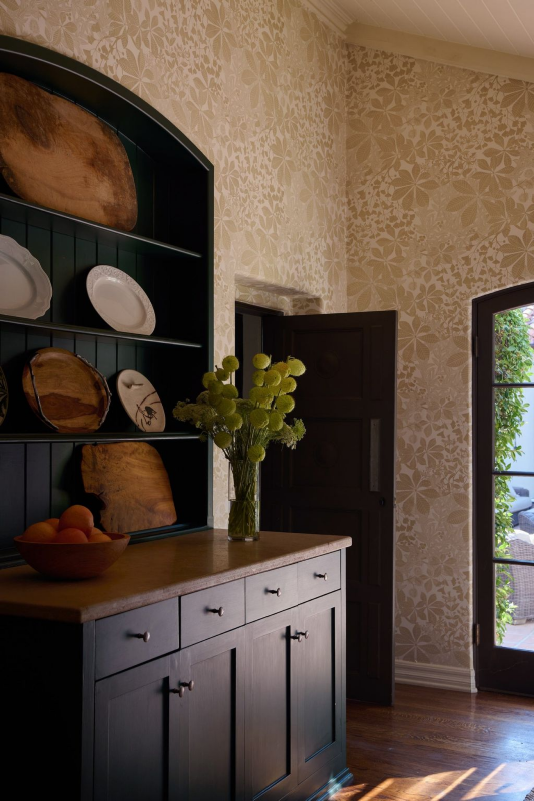 These rich tones of the kitchen are softened by the more feminine touch of the tan floral wallpaper that lines the walls.