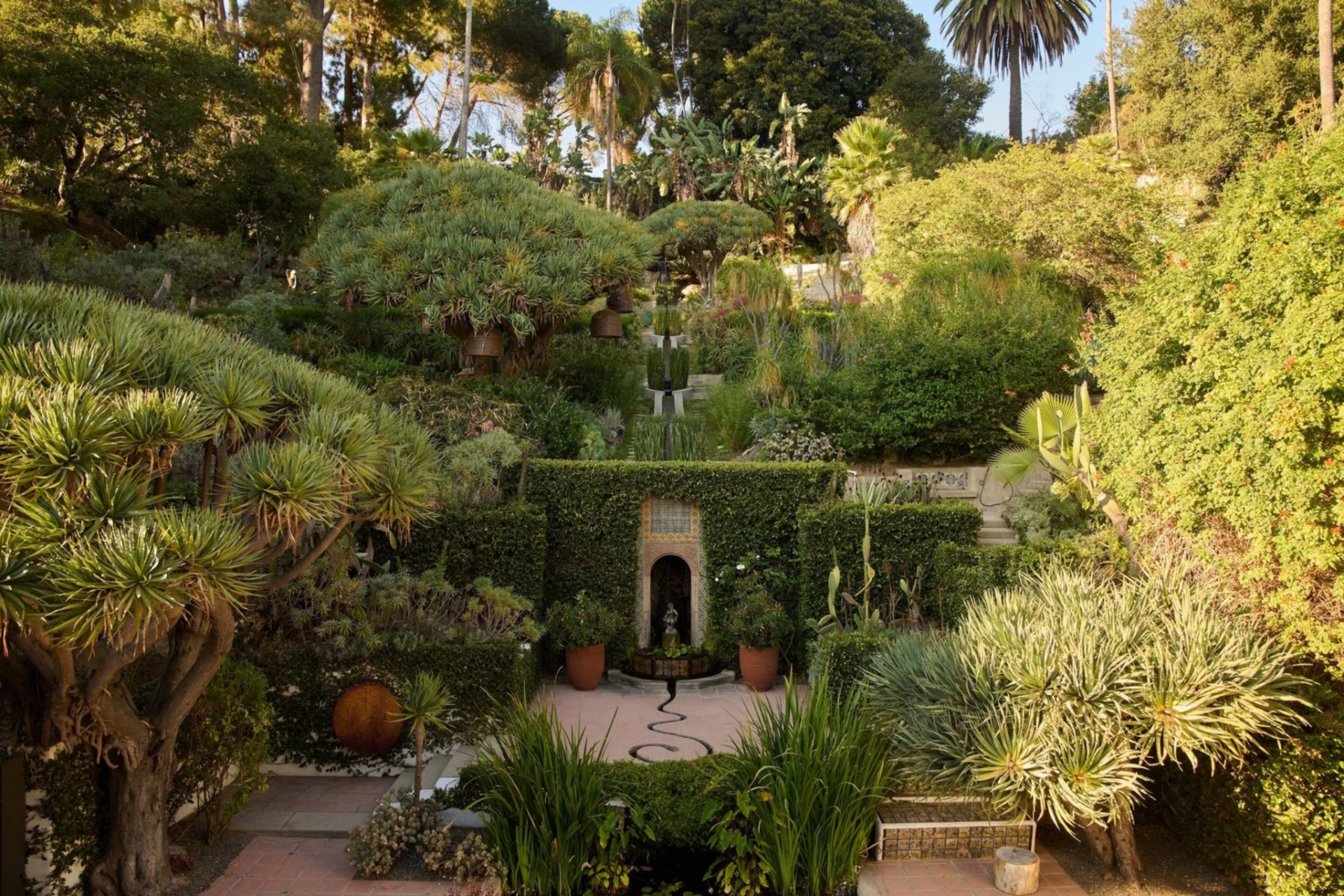 Spread across the hillside, the grounds unfold as a series of intimate outdoor spaces, connected by winding paths, stone terraces, and layered landscaping.