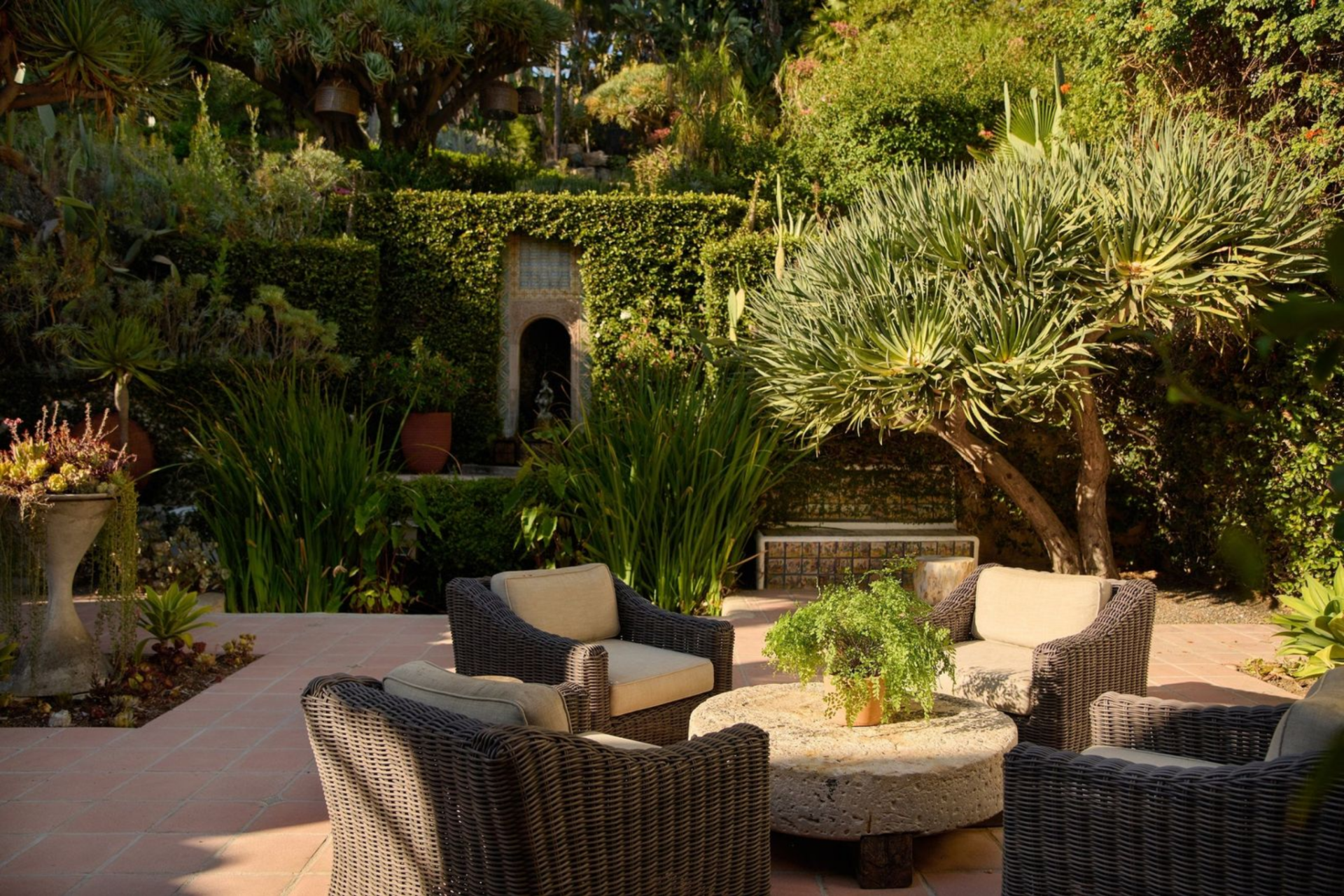 Woven seating clusters around a low stone table, creating a natural gathering spot that feels tucked away yet open to the surrounding greenery.