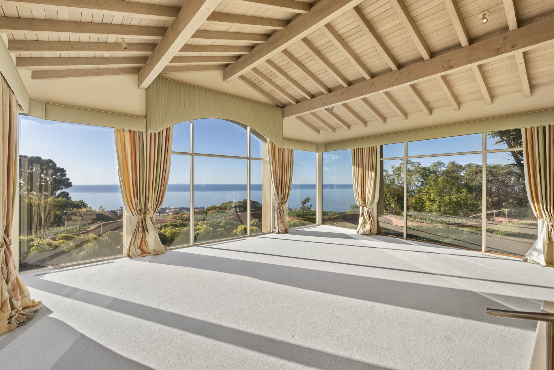Exposed, whitewashed beams stretch overhead, adding warmth and structure to the living area's ceiling, while walls of glass wrap the room and pull the Pacific straight into view. 