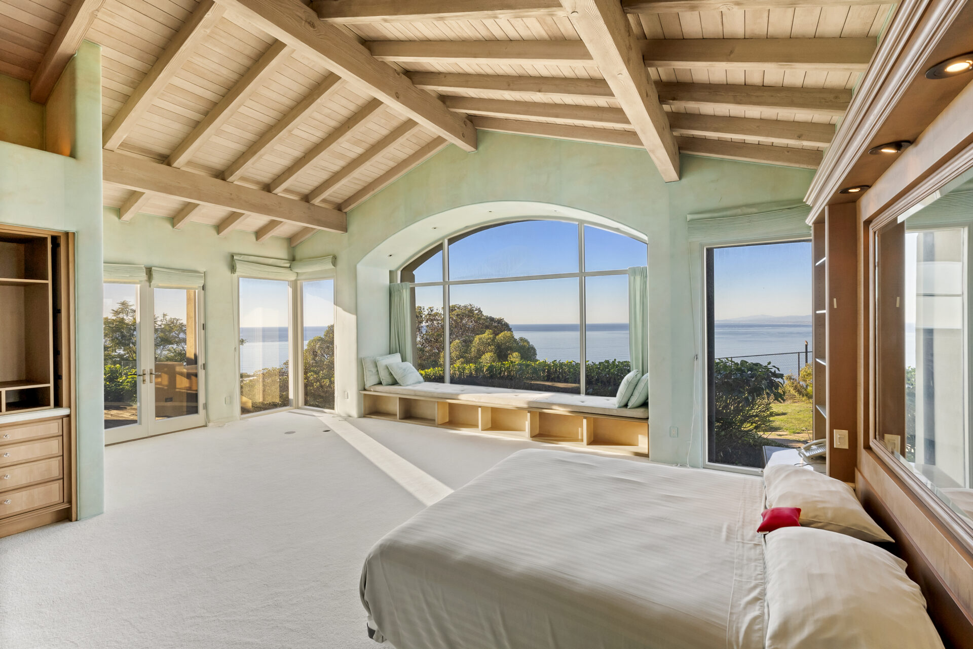 Primary suite where more exposed wood beams stretch overhead, their pale finish warming the space, while soft seafoam walls and neutral carpeting keep the focus on the view. 