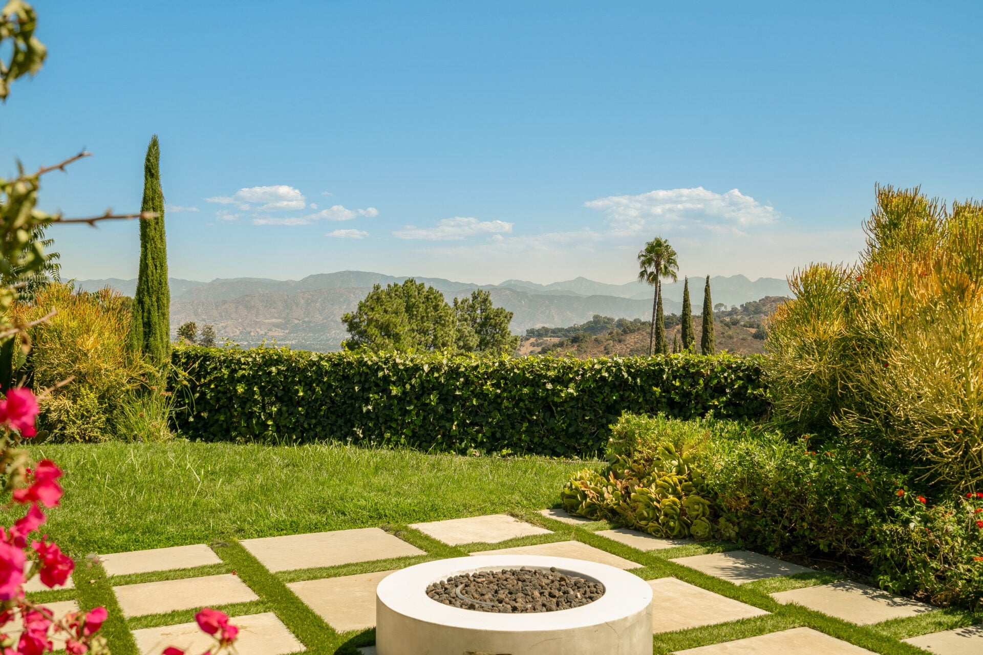 Outdoor fireplace surrounded by greenery overlooking the mountains.