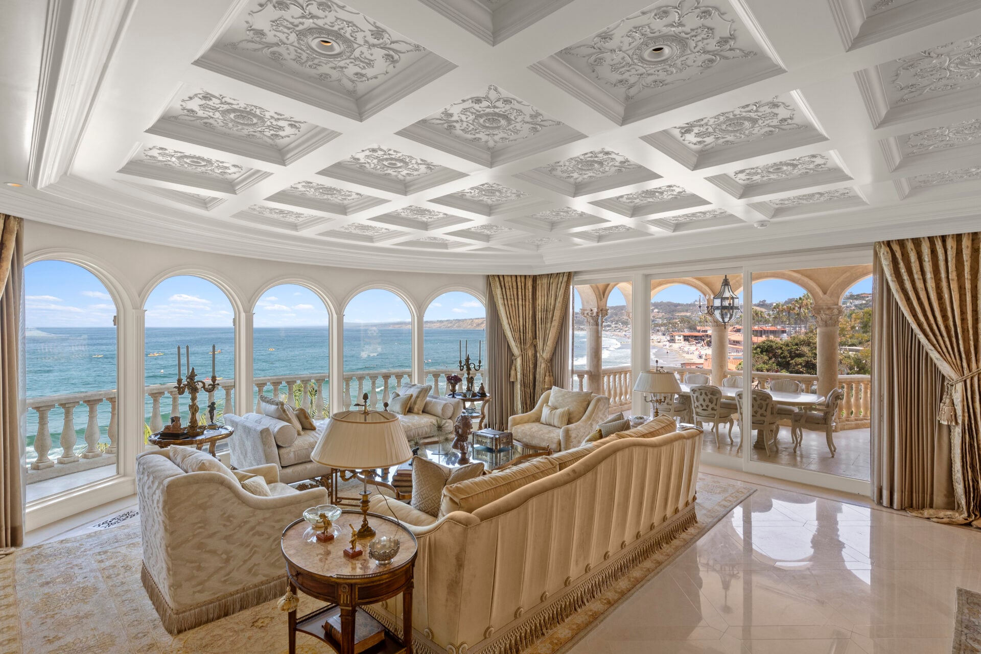 Polished stone floors reflect the natural light, while sliding doors open to a columned loggia set up for outdoor dining, extending the living space outward toward the ocean.