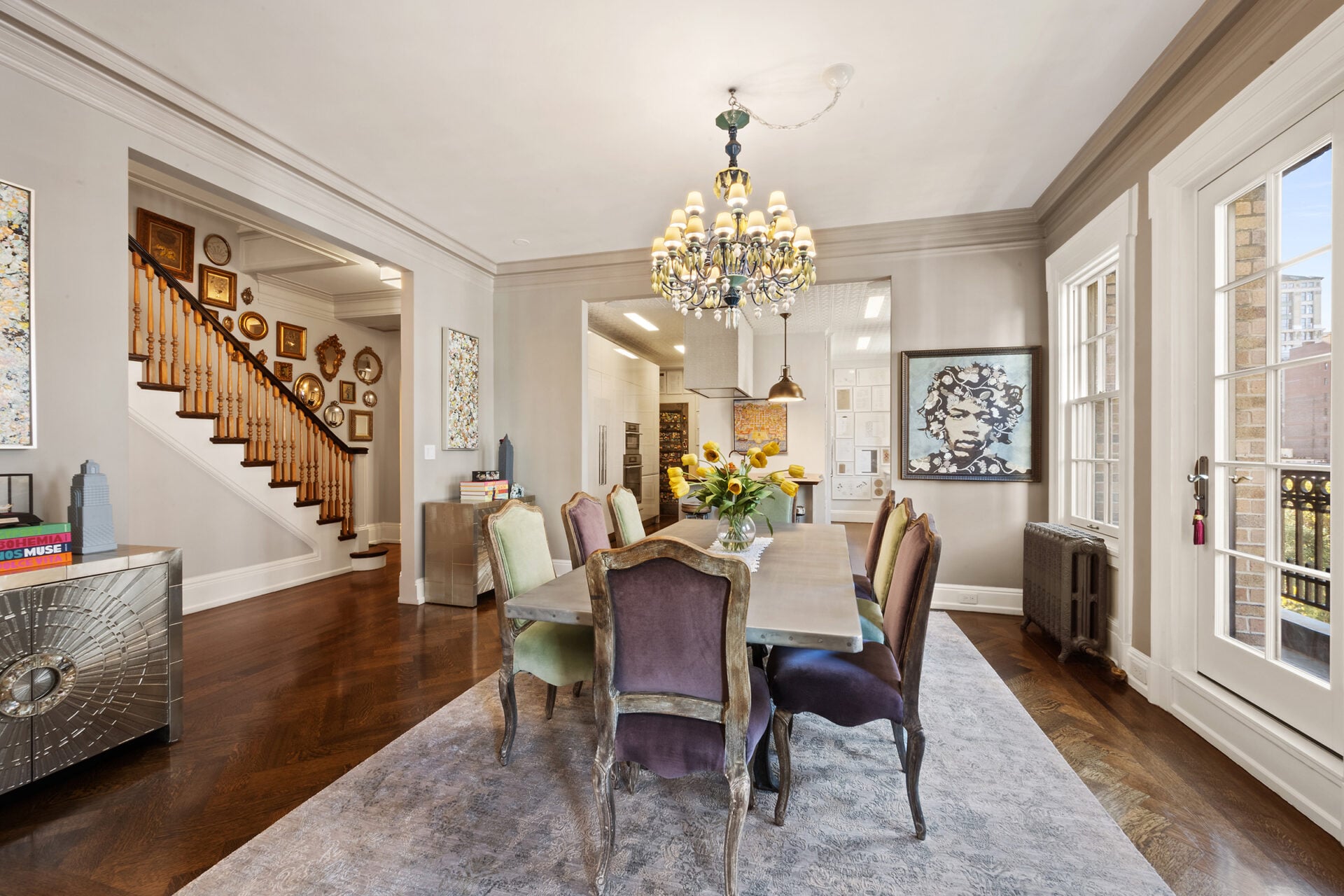 A long dining table sits centered on a soft area rug, surrounded by upholstered chairs, while crown molding and wide-plank floors reinforce the classic Manhattan proportions. 