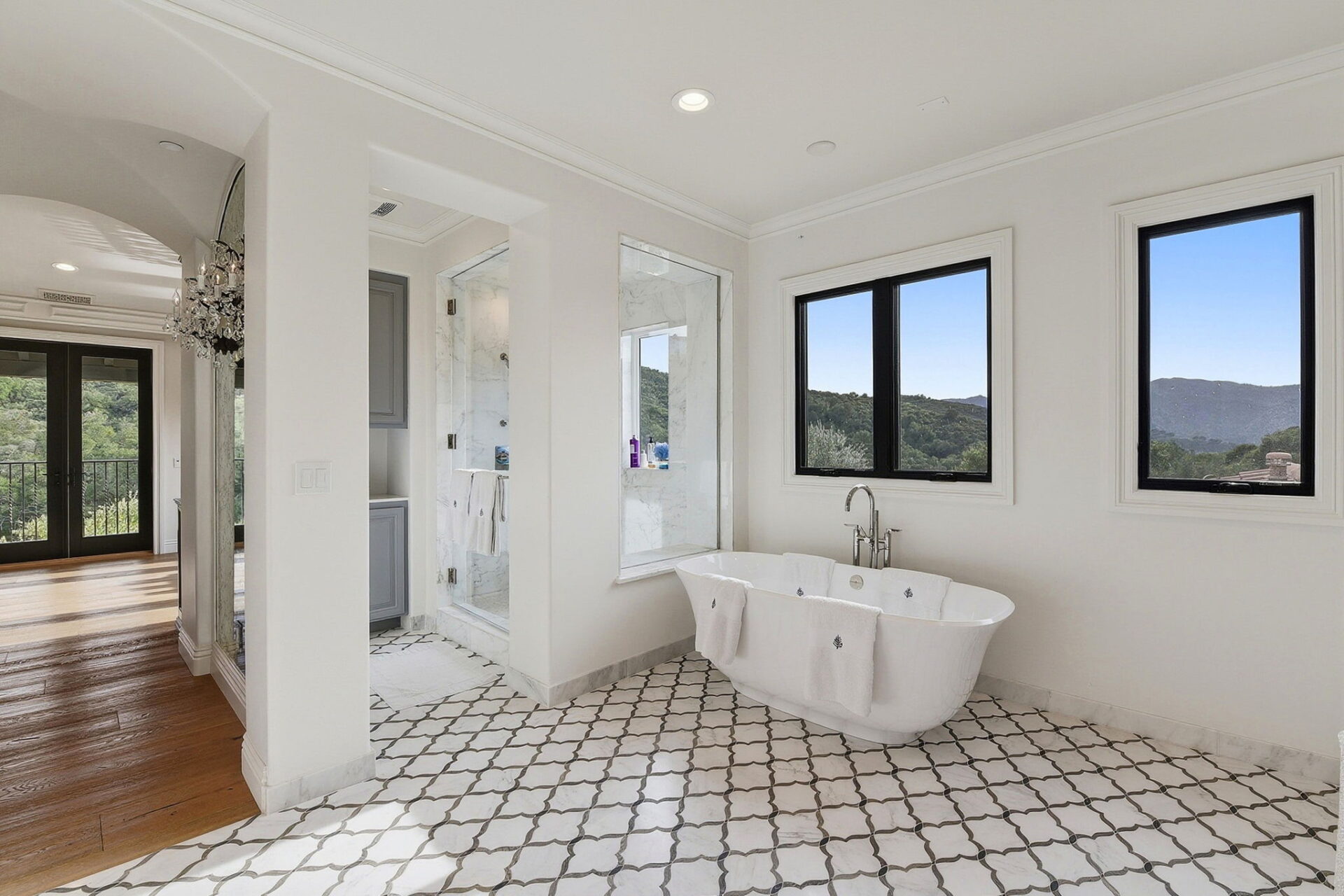 To one side, a freestanding soaking tub sits beneath picture windows framing mountain views.