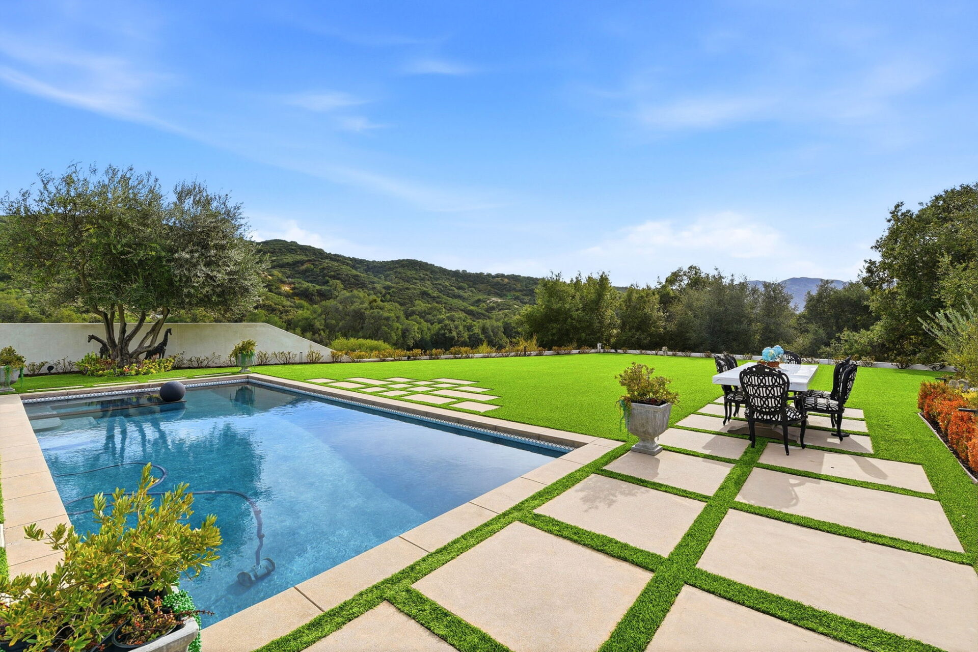 The resort-style pool stretches toward a wide expanse of manicured turf, reflecting the sky and surrounding hills.