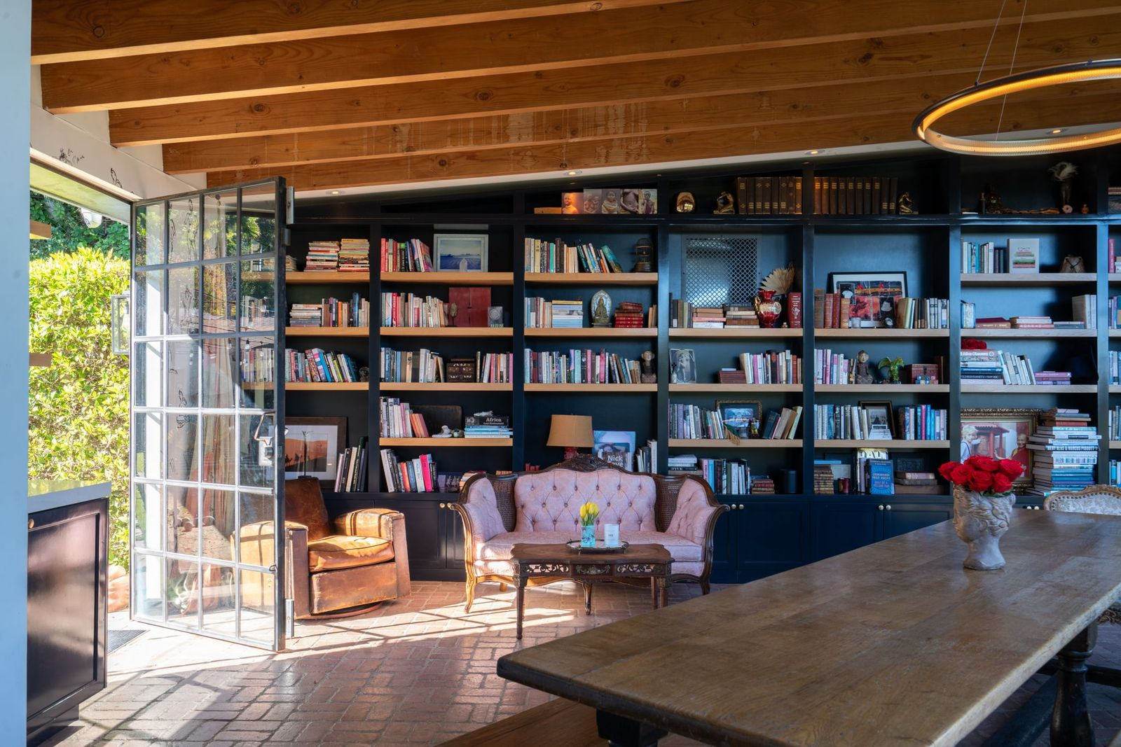 Seperate from the main house, the library salon sits along a built-in shelving, painted dark to contrast with the light wood ceiling beams overhead. 