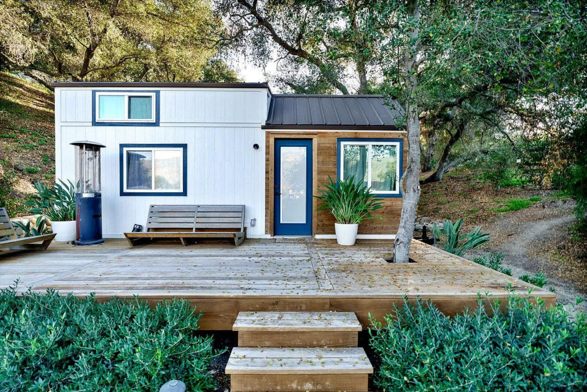 A tiny house set within the shade of trees on a wood deck.