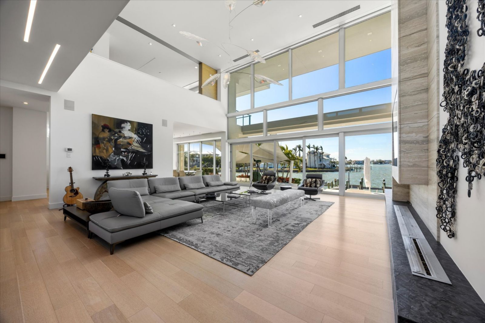 The home opens into a light-filled great room defined by soaring ceilings, walls of glass, and pocketing sliders that disappear to connect the interior directly to the water beyond. 