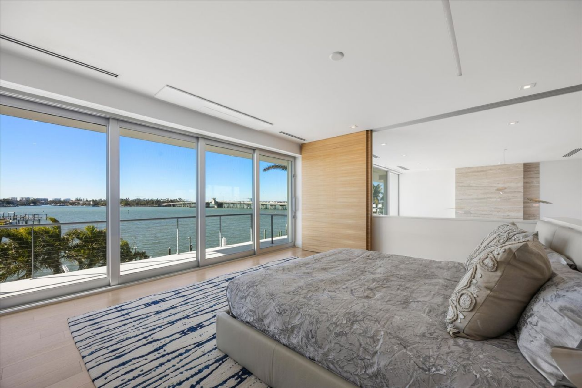 The bedroom is arranged in an open, loft-style layout where floor-to-ceiling glass runs the length of the wall, framing the water and sliding open to a private terrace. 