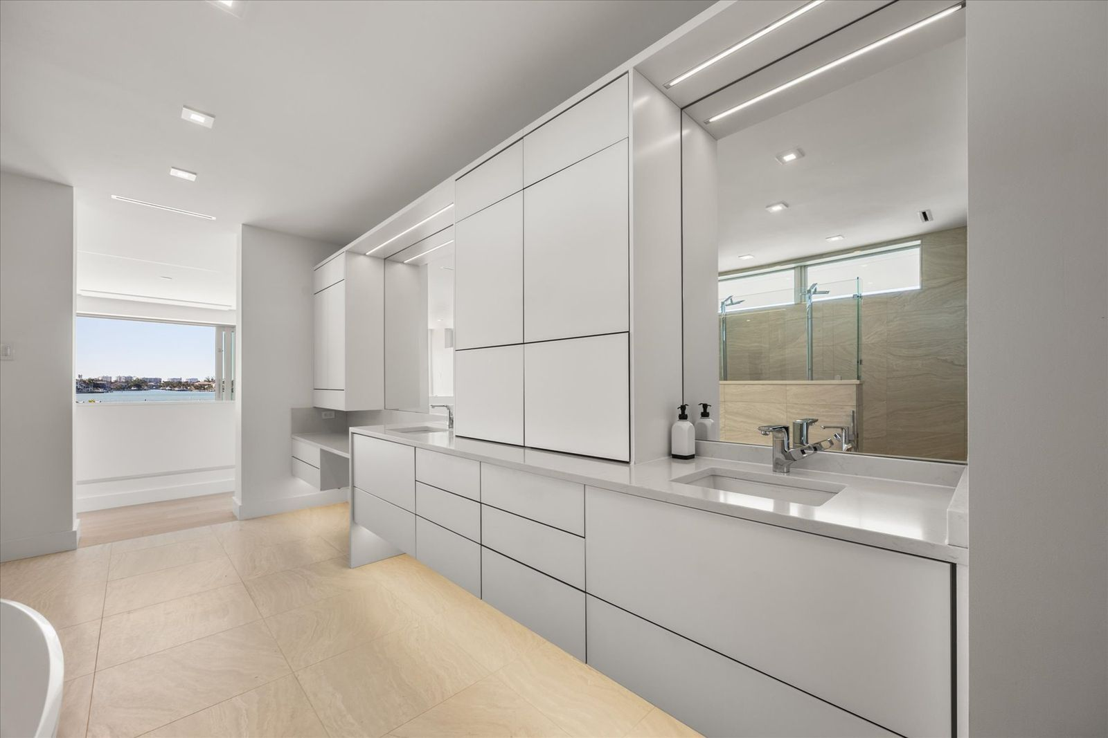 The shower enclosure stretches wide with multiple glass panels, while the floating vanity and integrated cabinetry keep the space feeling uncluttered. 